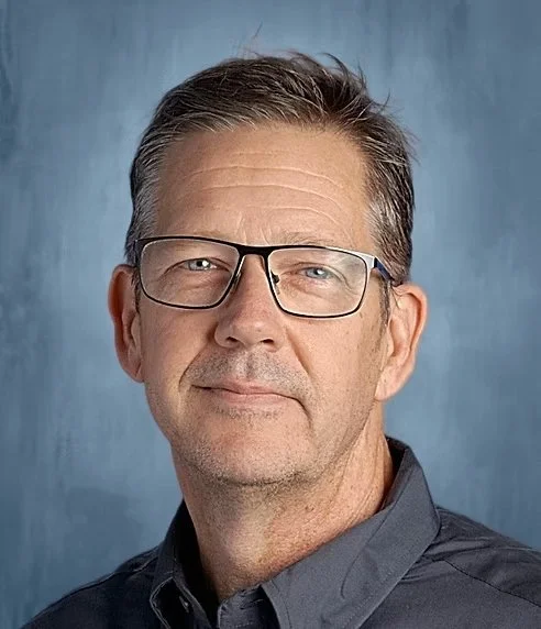 Portrait of a man wearing glasses and a gray collared shirt against a blue background