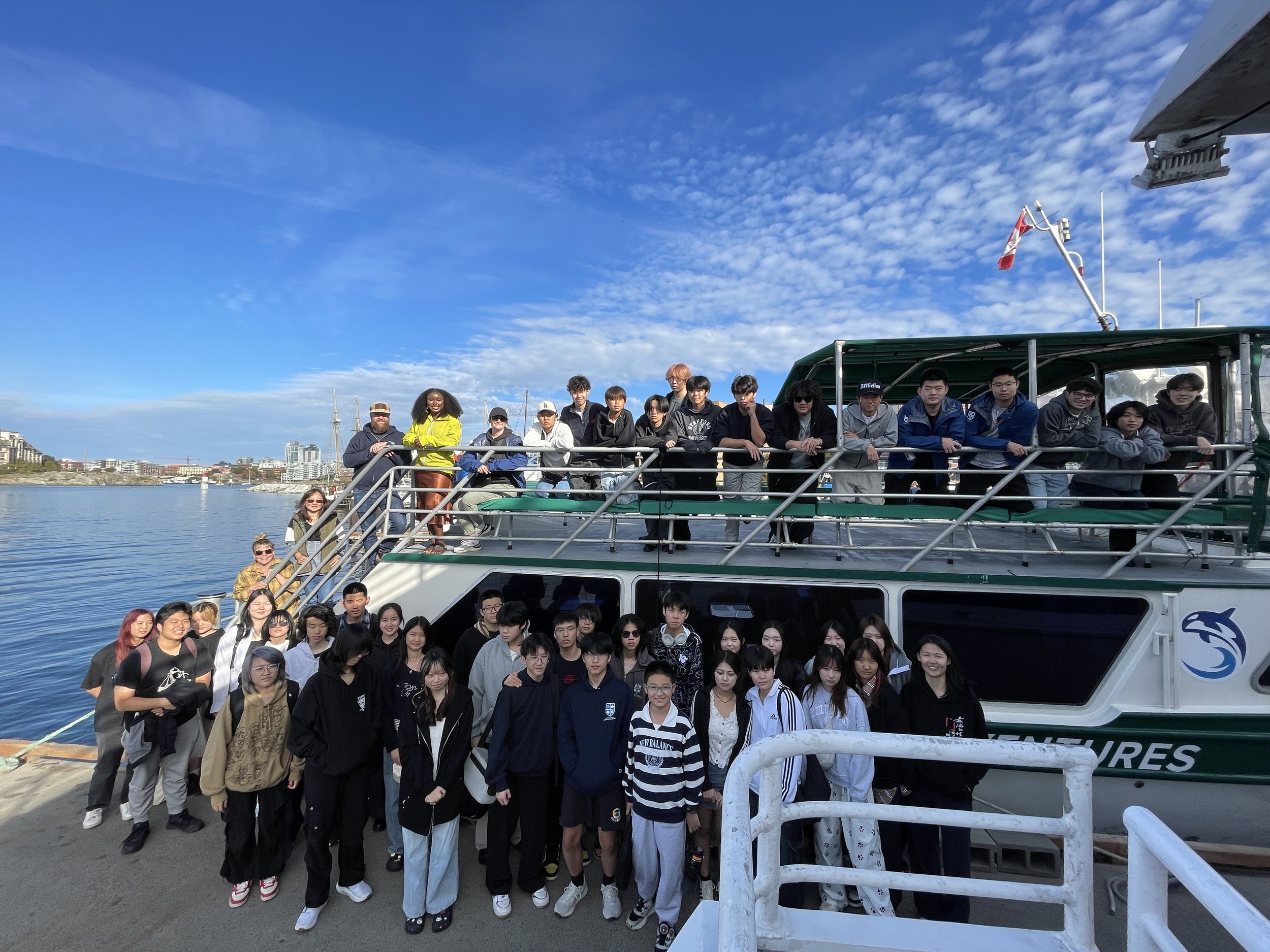Large group posing on the deck of a passenger boat in a harbor under a bright blue sky