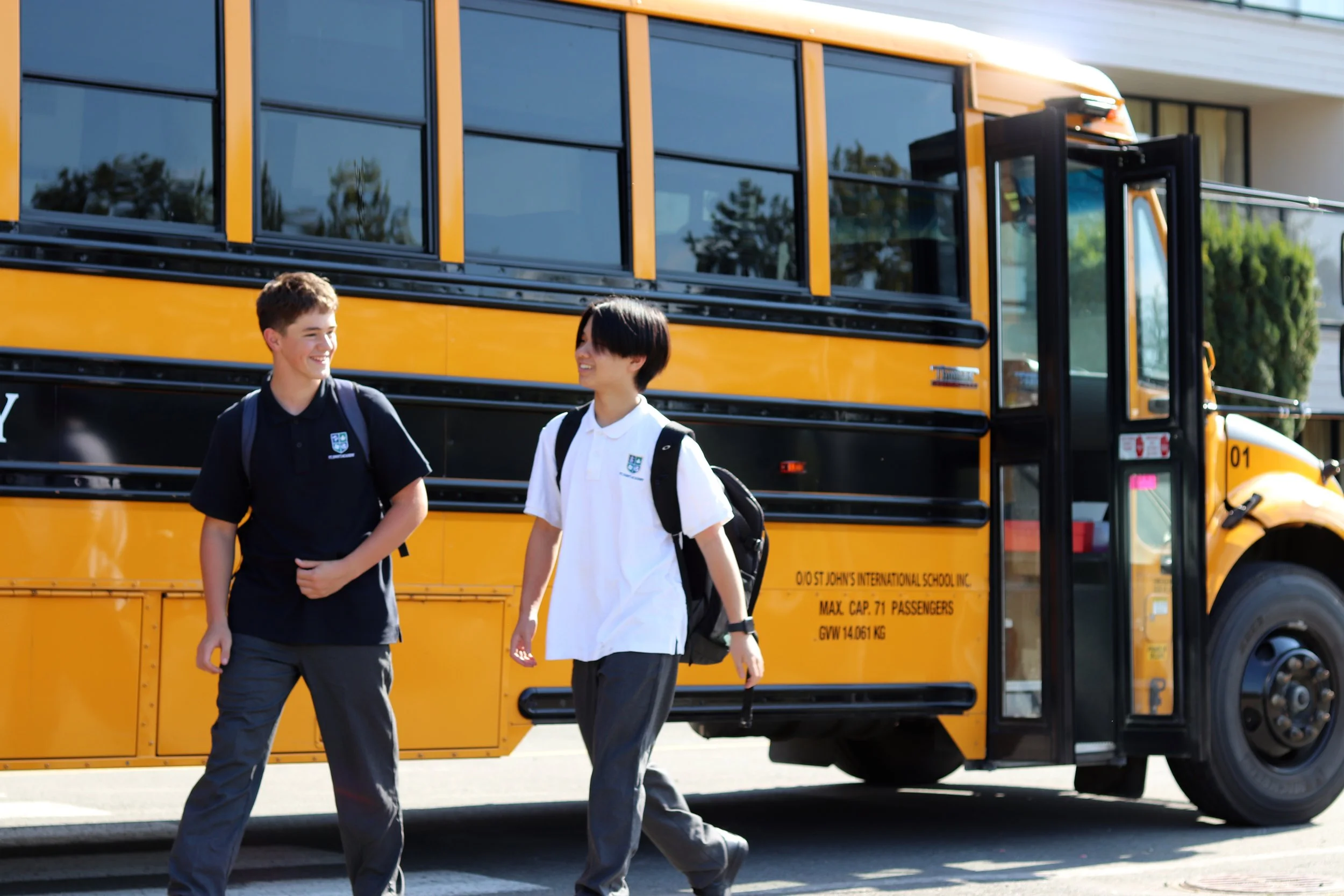 Two uniformed students with backpacks walking in front of a yellow school bus