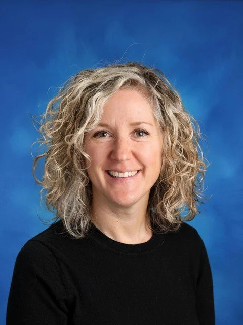 Smiling woman with curly blonde hair wearing a black shirt against a blue studio background