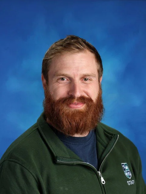 Photo of a man wearing a green staff jacket against a blue background