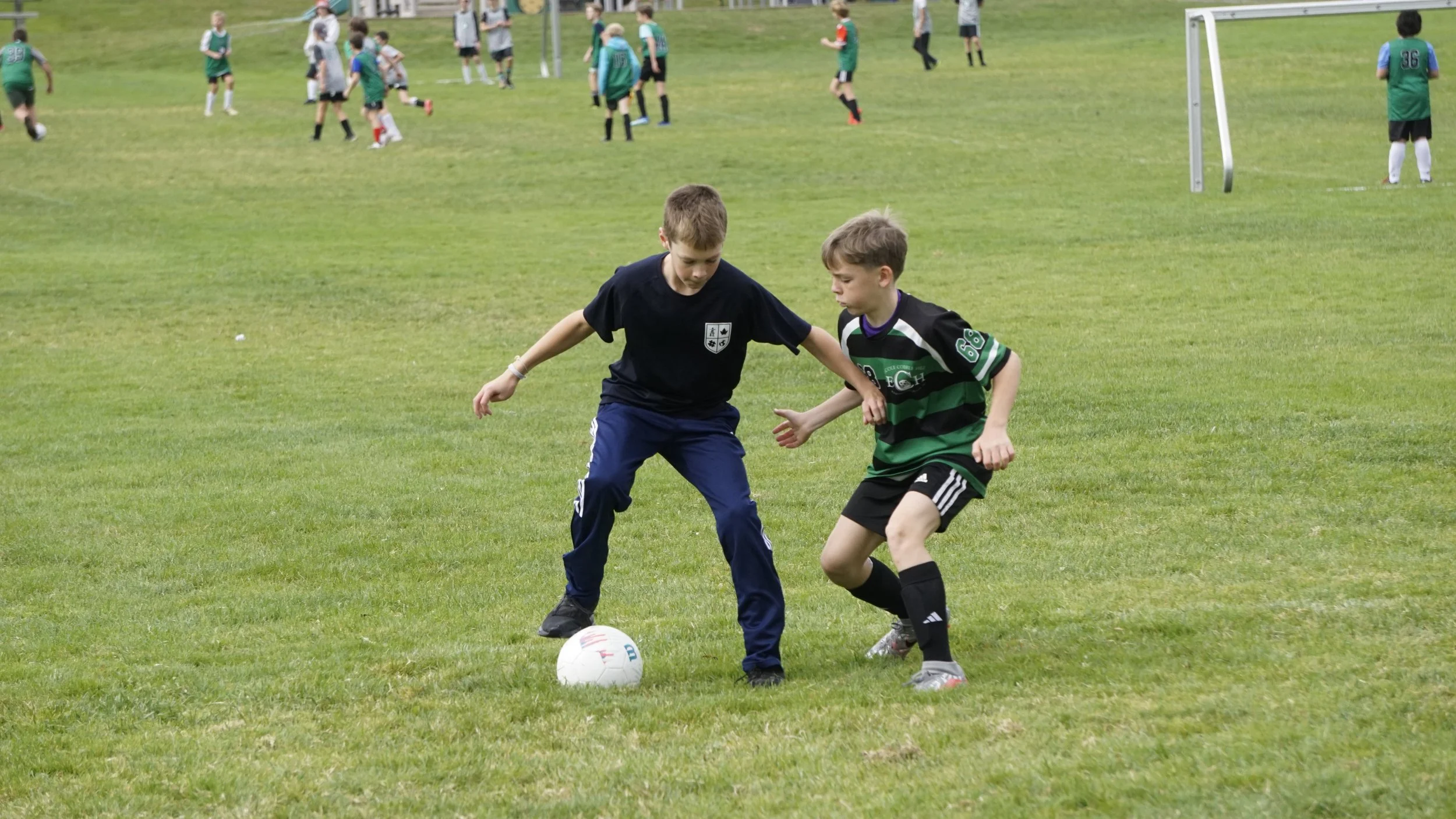 Two boys compete for the ball during a youth soccer game on a grassy field.