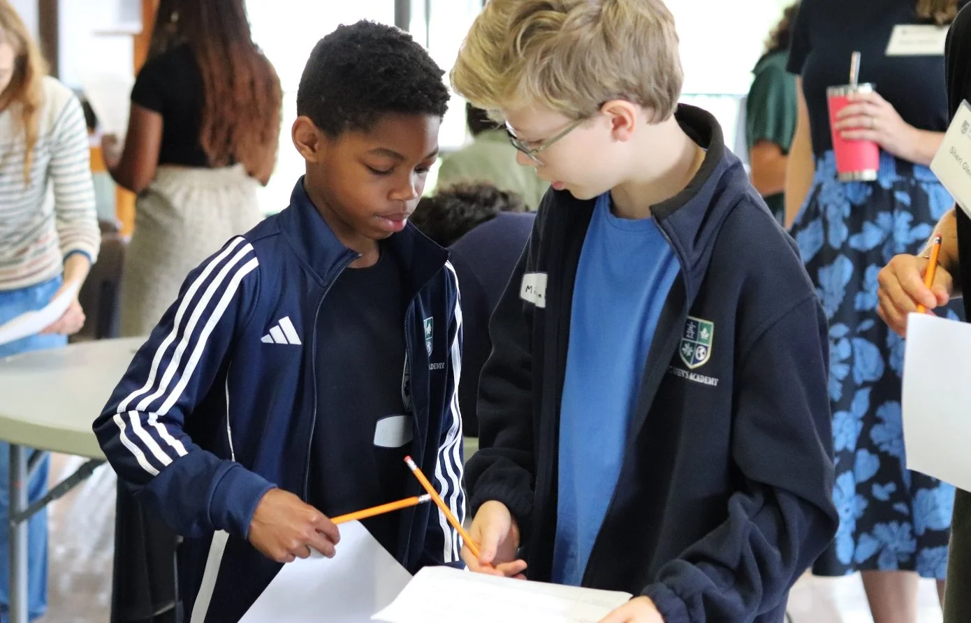 Two schoolboys in athletic jackets work together on a worksheet with pencils at a school event.