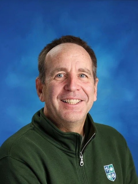 Smiling middle-aged man in a green zip-up jacket posing against a blue background