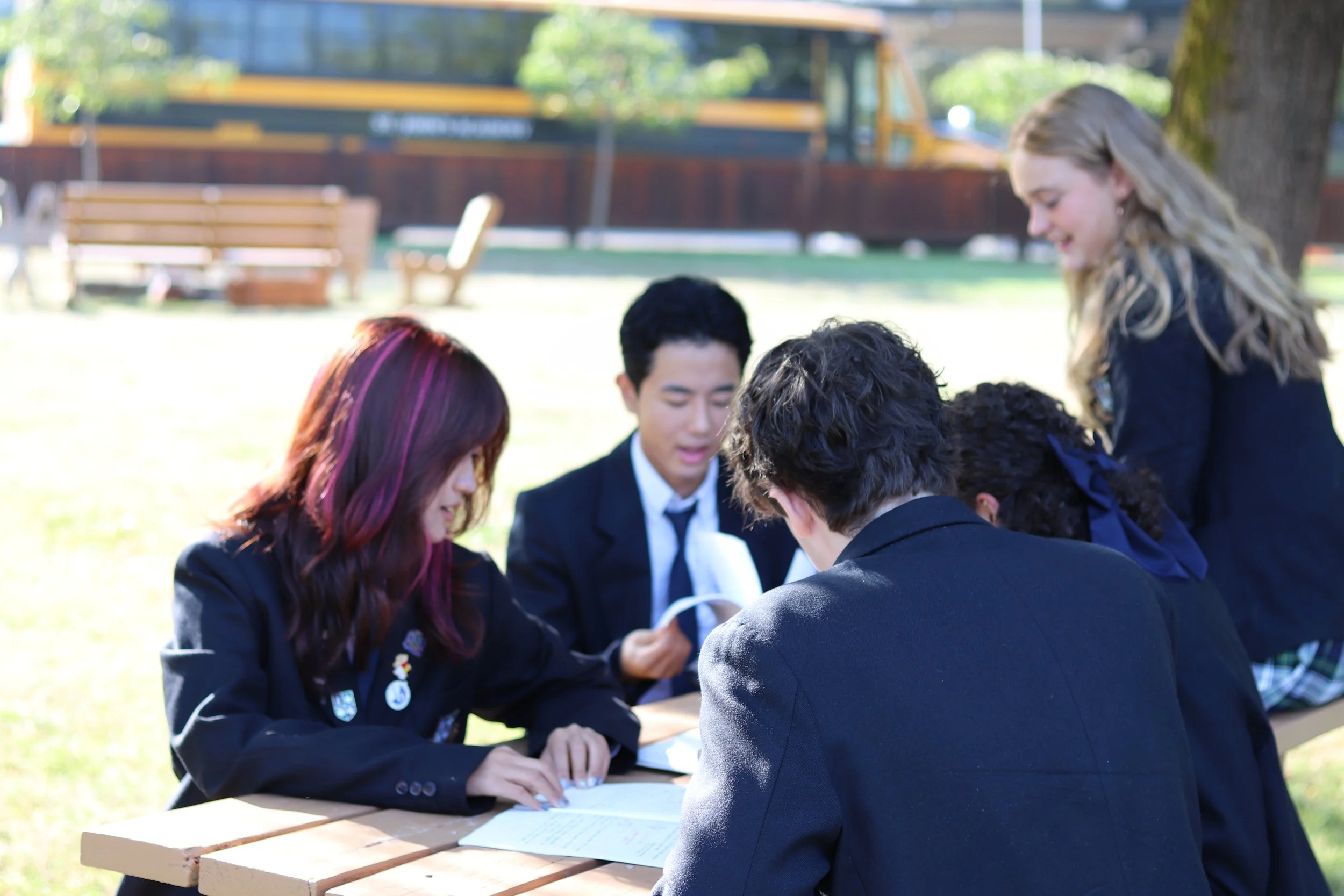 Group of students in formal attire collaborating around a picnic table outdoors
