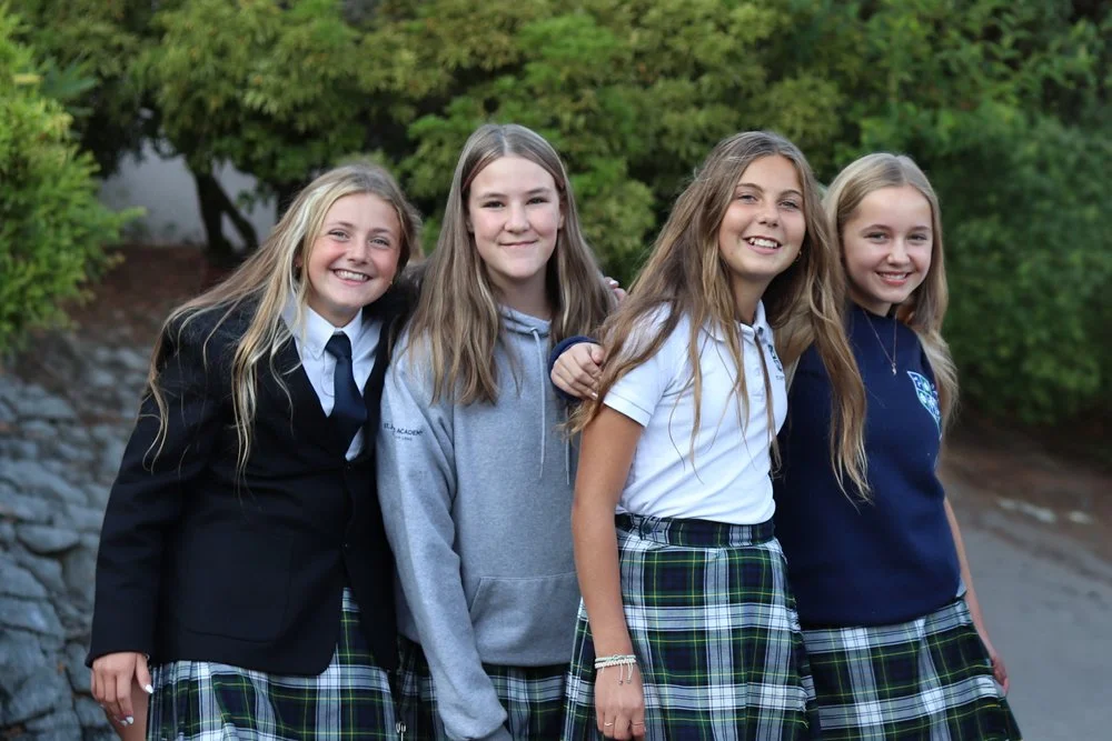 Four smiling schoolgirls in uniforms posing together outdoors.