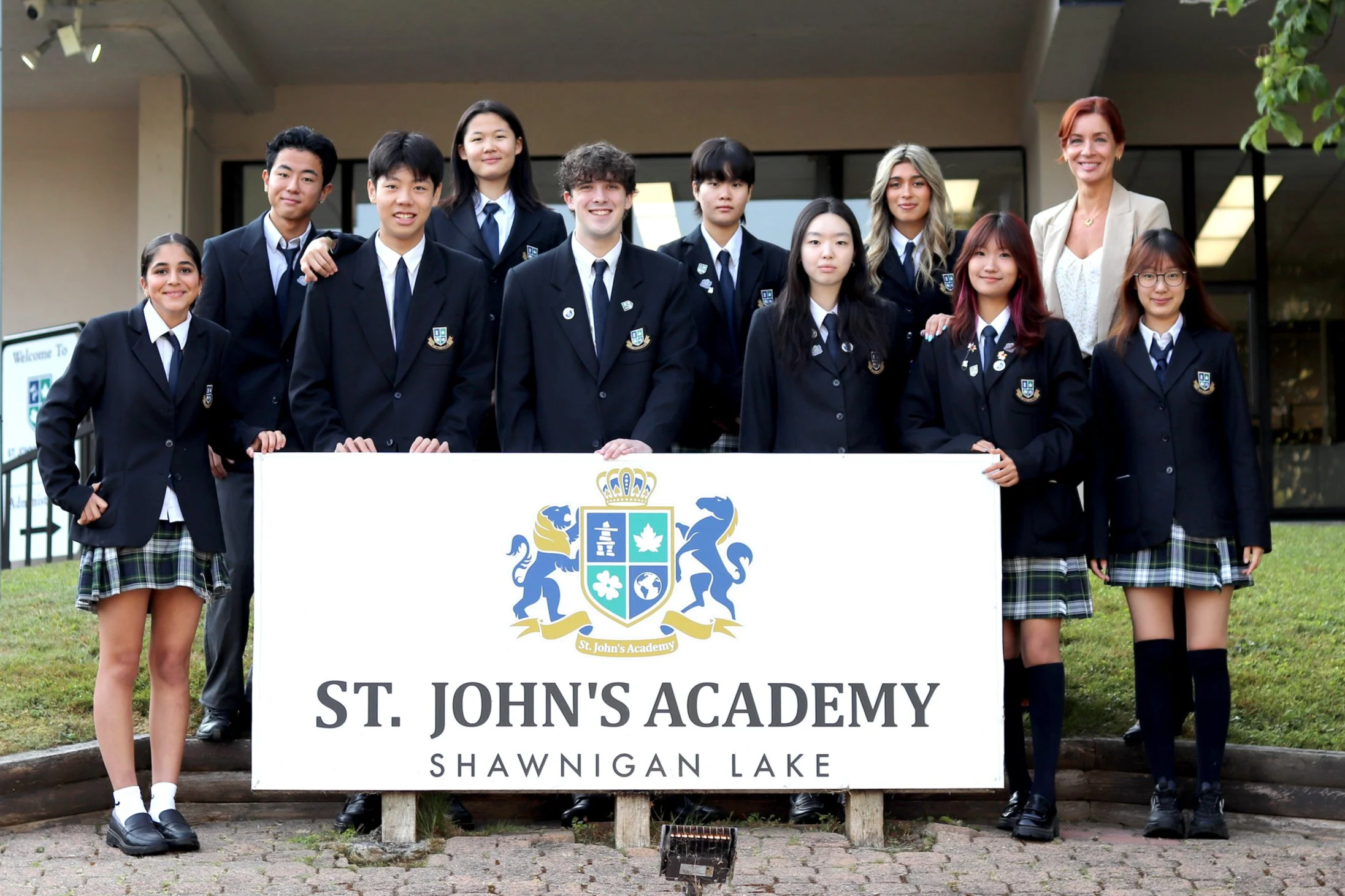 St. John's Academy Shawnigan Lake students and teacher posing in school uniforms behind a campus sign.