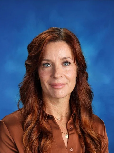 Portrait of a smiling red-haired woman in a brown blouse against a blue background