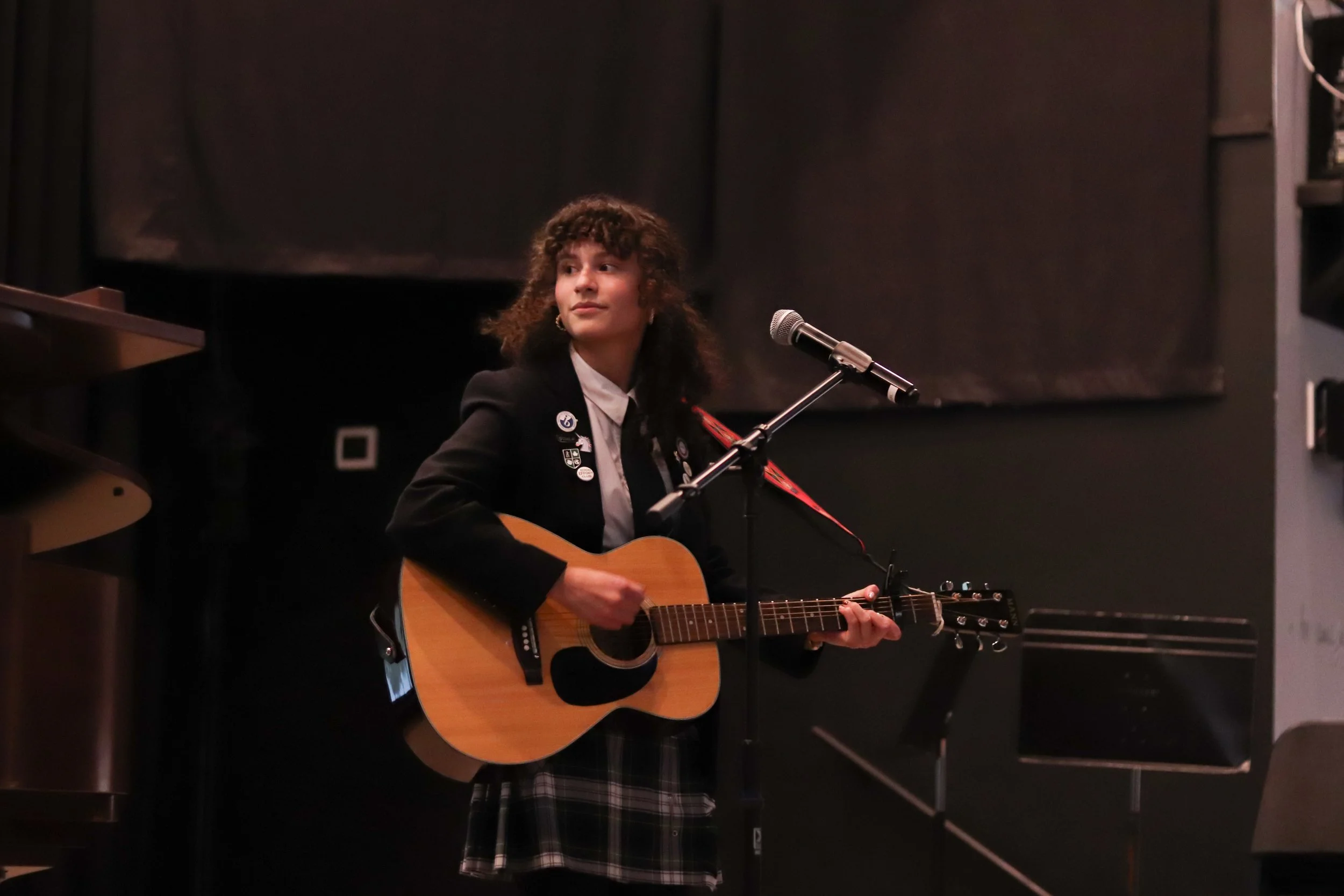 Musician in a school uniform playing an acoustic guitar and singing into a microphone onstage