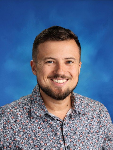 Smiling man in a patterned shirt against a blue background