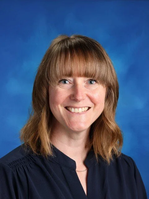 Professional headshot of a smiling woman with brown hair and bangs against a blue background