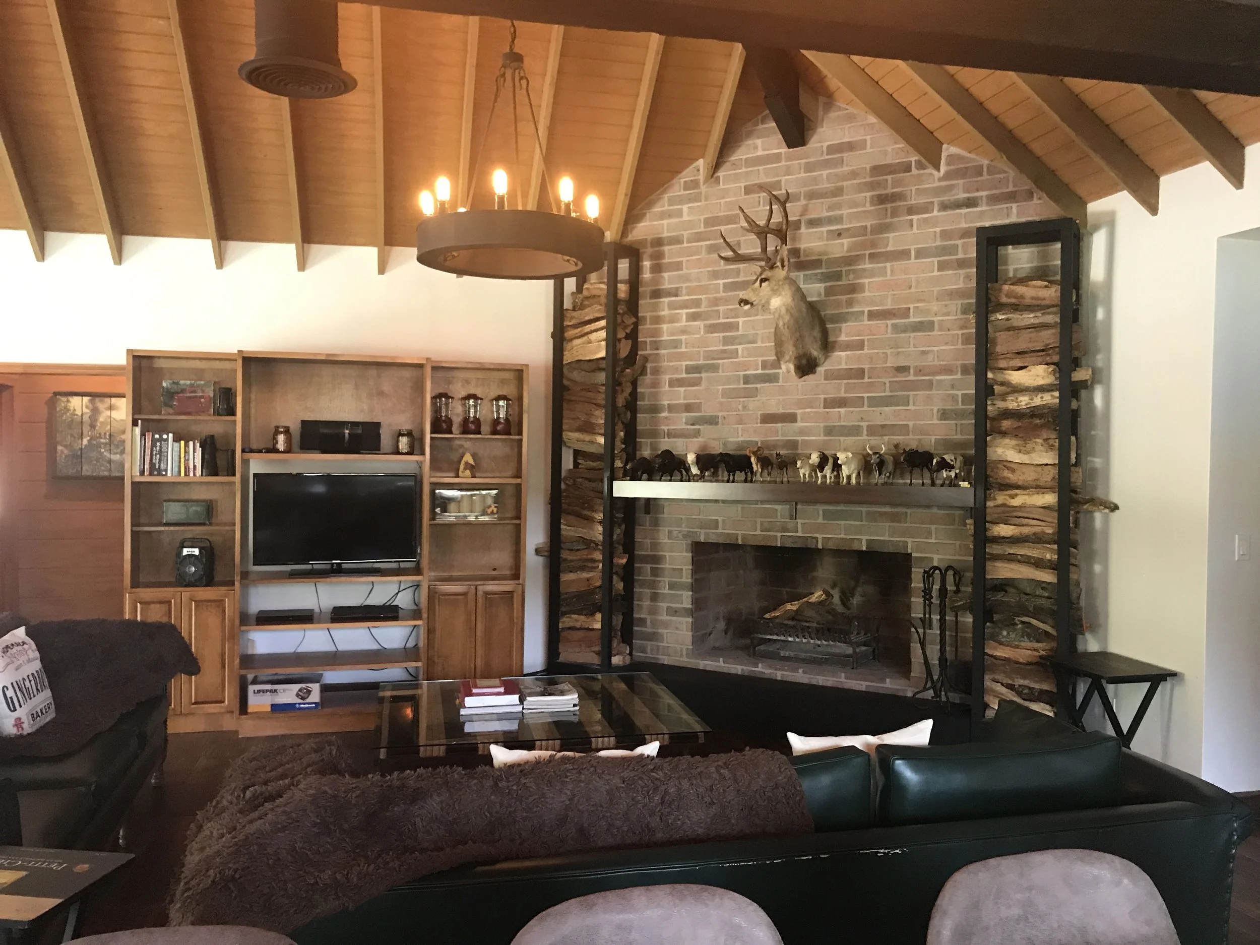 Living room with brick fireplace, wooden ceiling beams, bookshelf, and seating area.