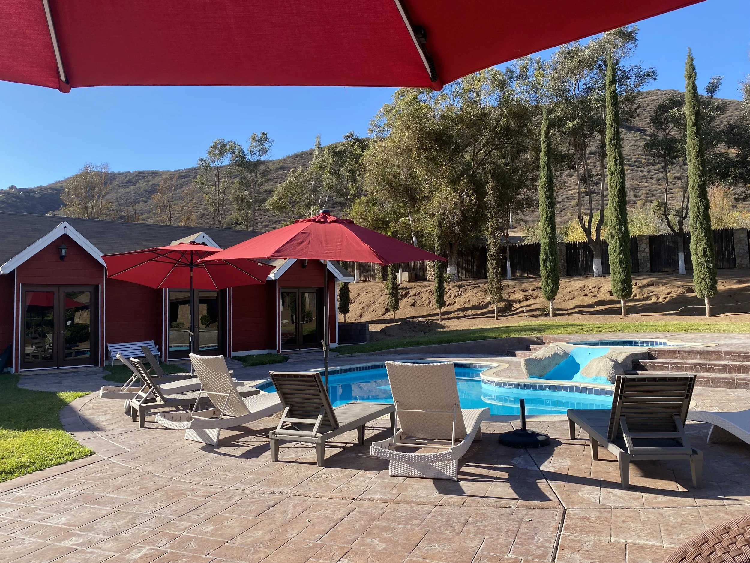 Private swimming pool, several lounge chairs, and red umbrellas, with views of trees and hills in the background.