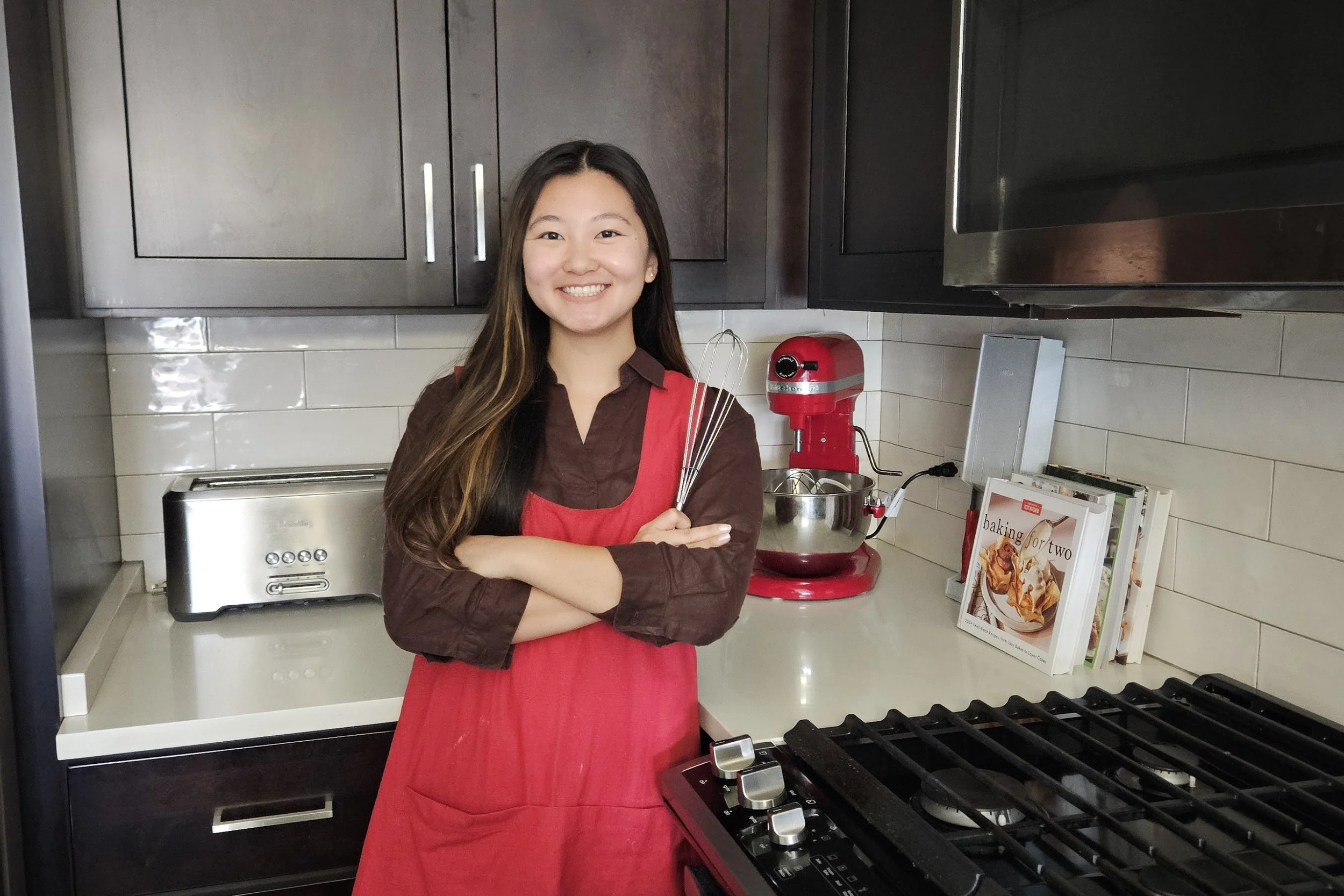 Jocelyn, the founder of Sweet Treats Bakery, posing with red apron and whisk.