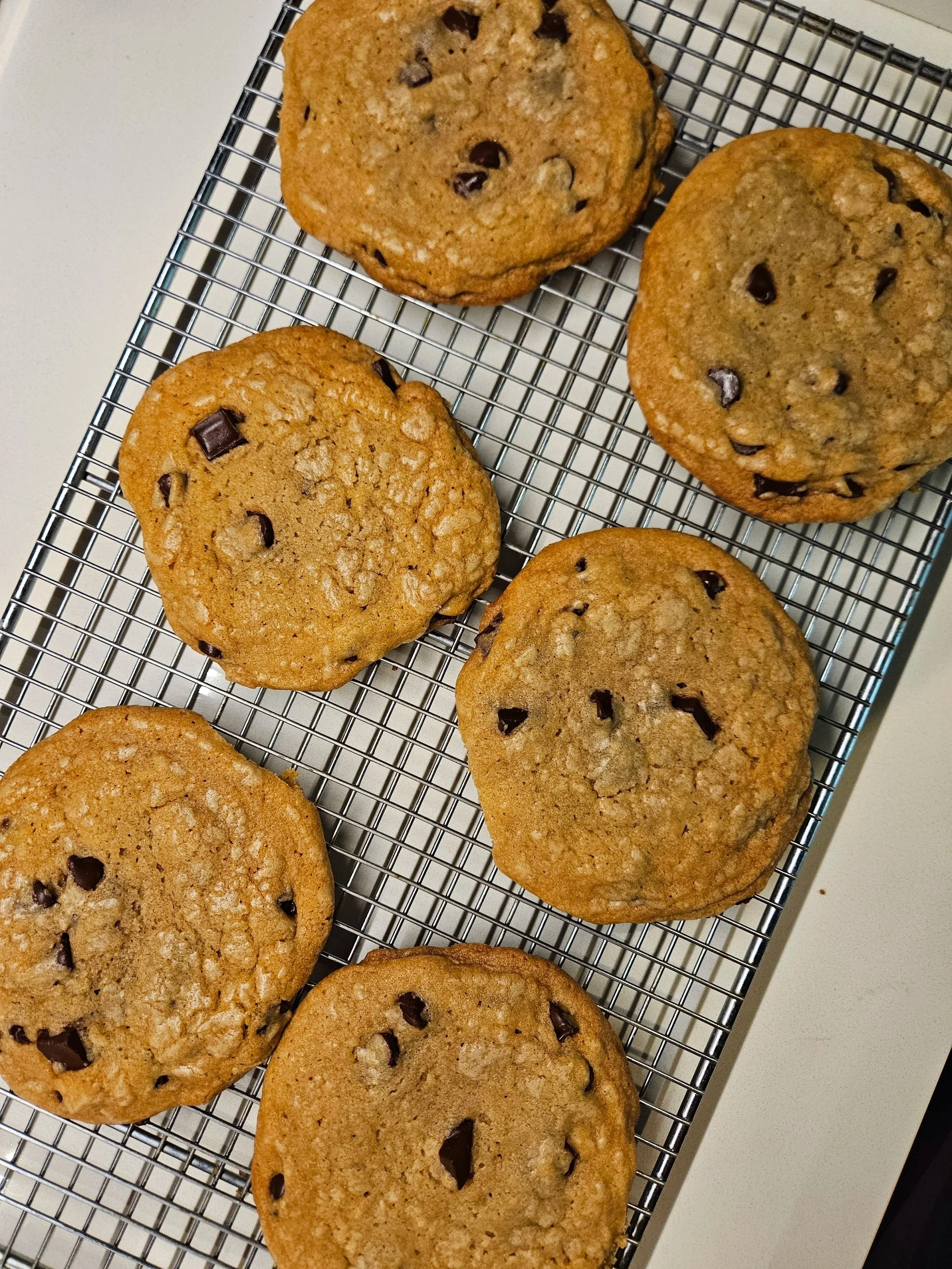 Six chocolate chip cookies cooling on a wire rack on a white surface.