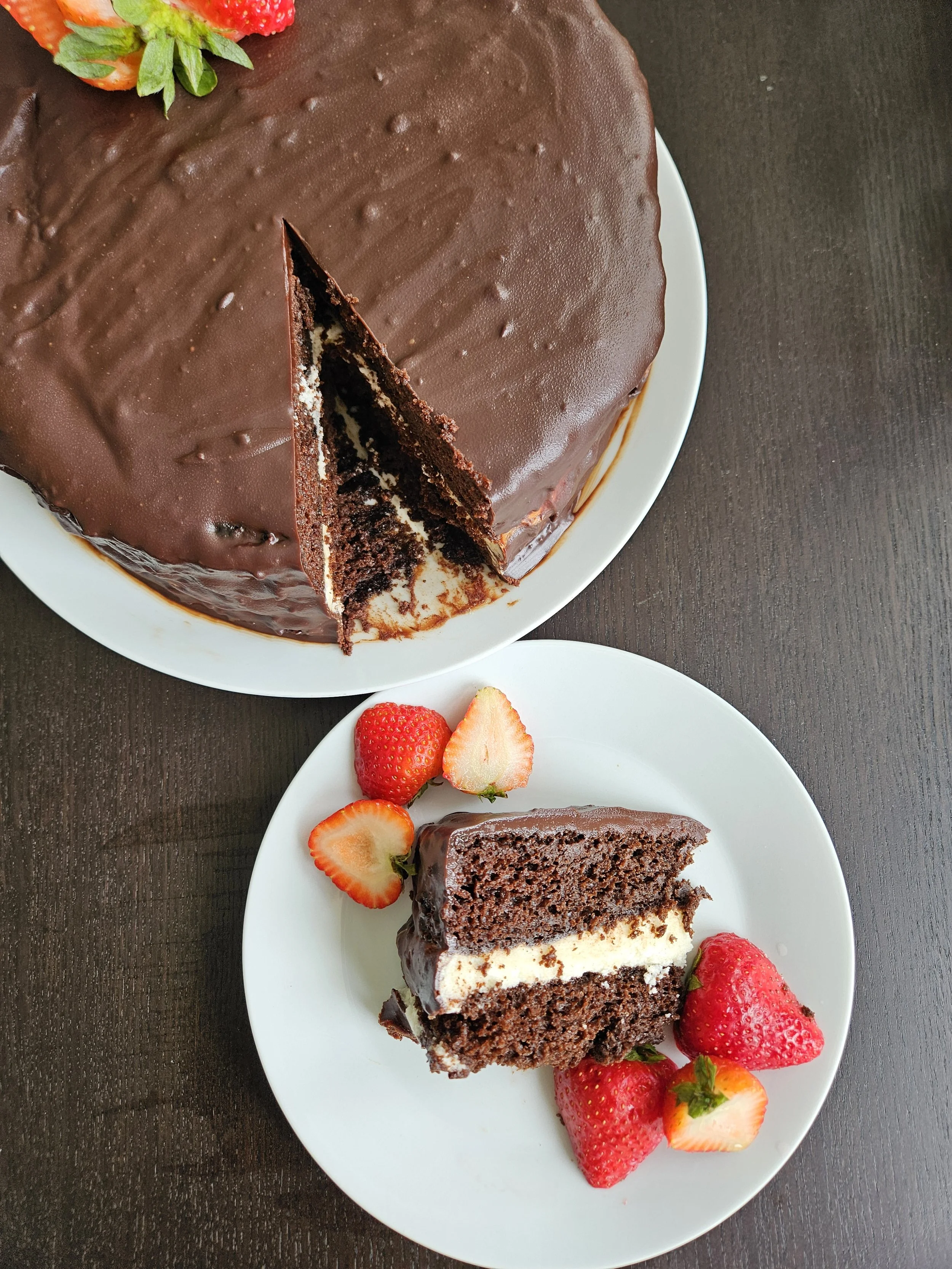 A chocolate layered cake with chocolate icing on top, decorated with strawberries, on a white plate.