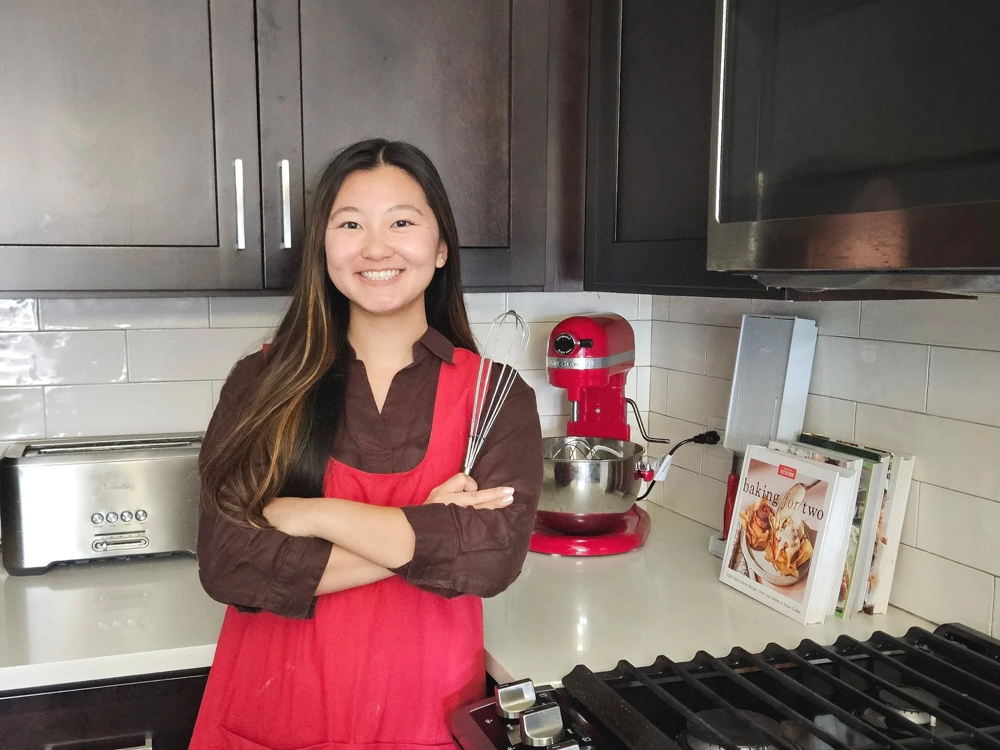 Jocelyn, the founder of Sweet Treats Bakery, posing with red apron and whisk.