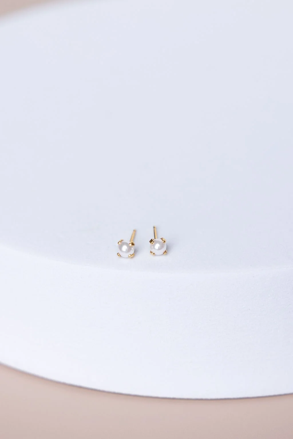 Pair of gold stud earrings with white pearl centers displayed against a light blue background.