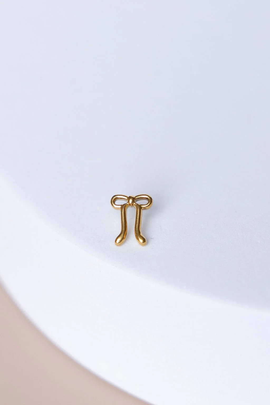 A small gold charm shaped like a pair of eyeglasses with a bow on top, placed on a white surface.