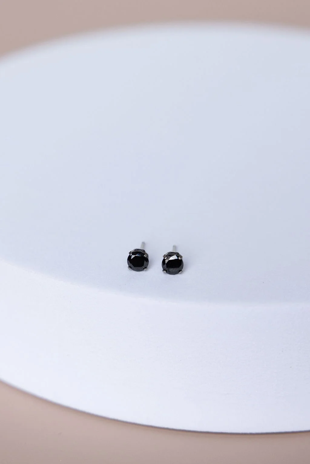 Pair of black gemstone stud earrings on a white curved surface.
