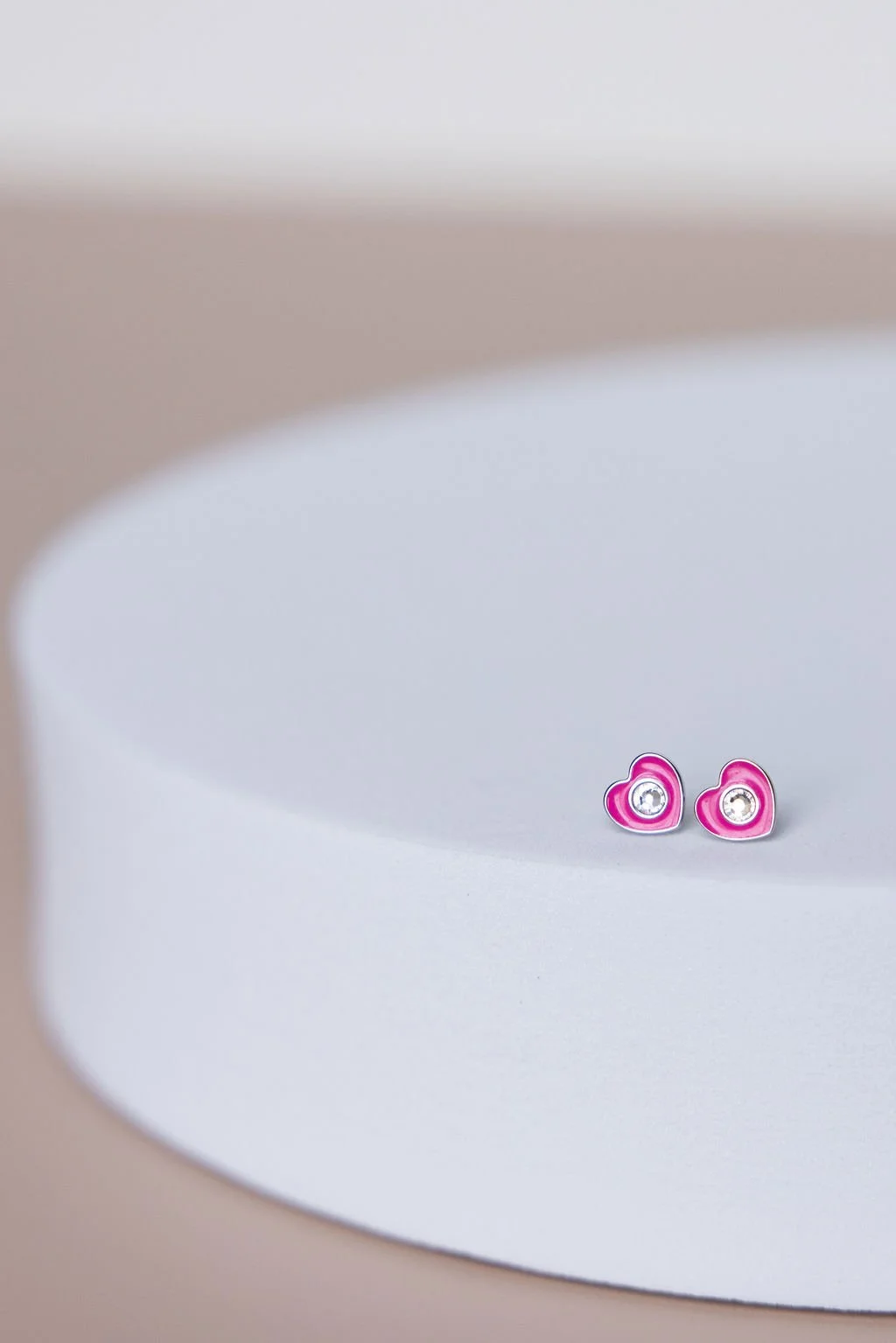 Pink heart-shaped earrings with small clear gemstones on a white surface.