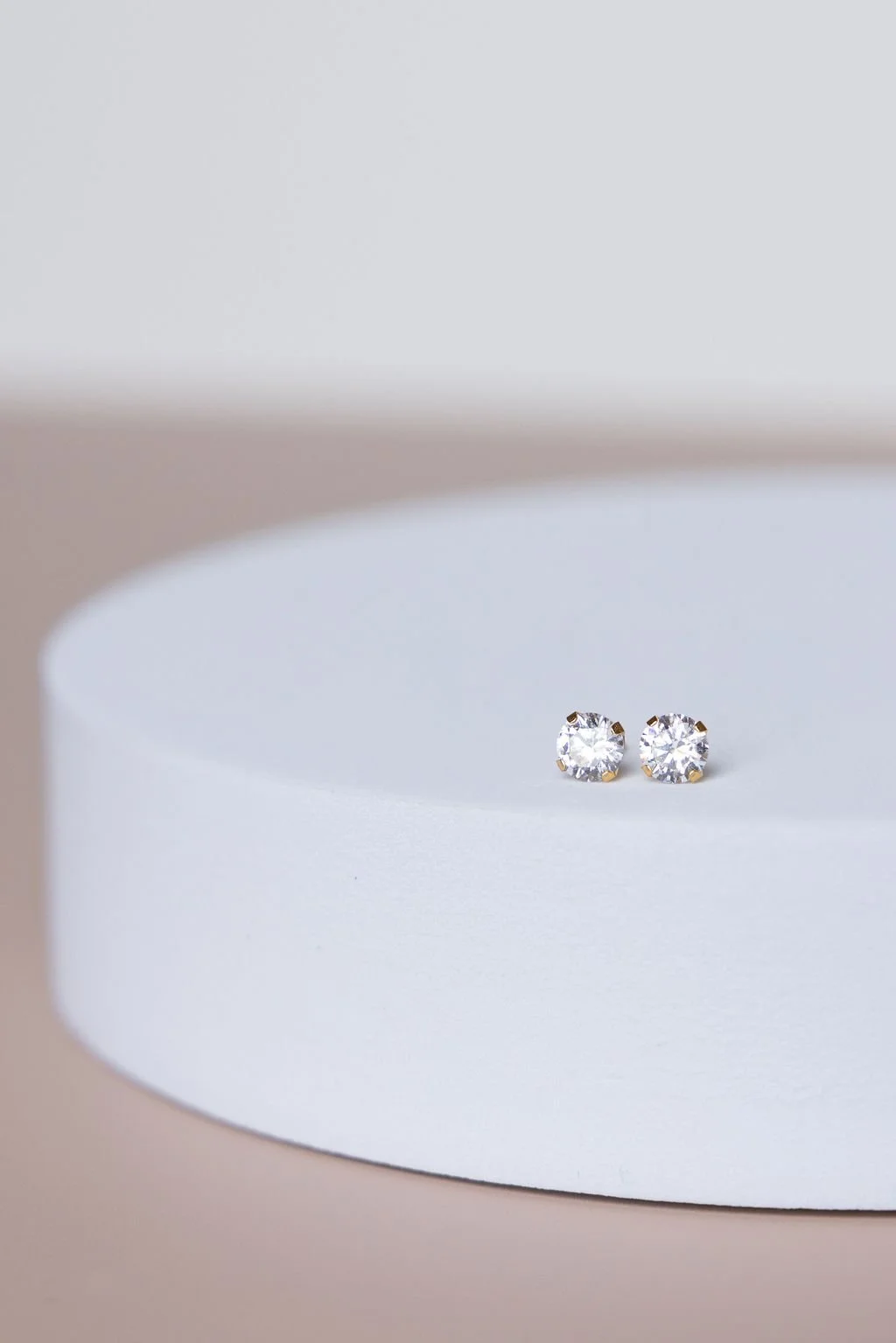 Pair of diamond stud earrings displayed on a white, curved surface with a minimalist background.