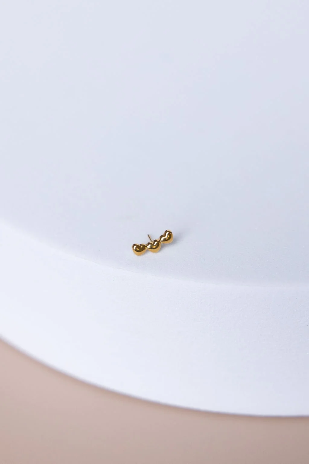 Small gold dangling earring on a white surface.
