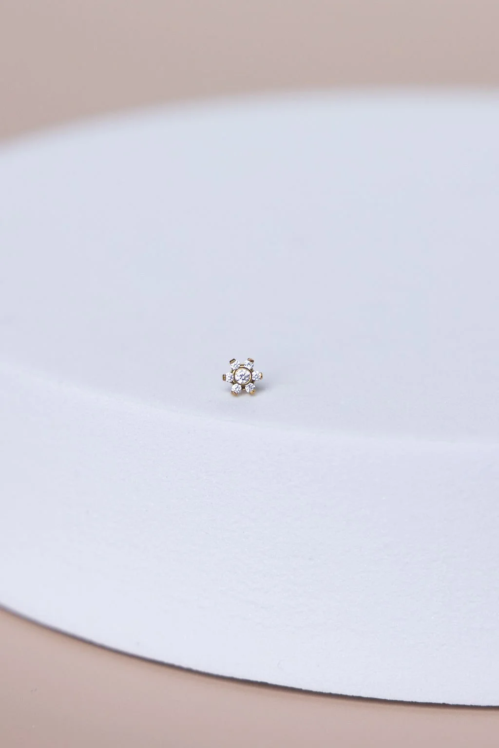 Close-up of a small silver and diamond flower-shaped earring on white fabric.