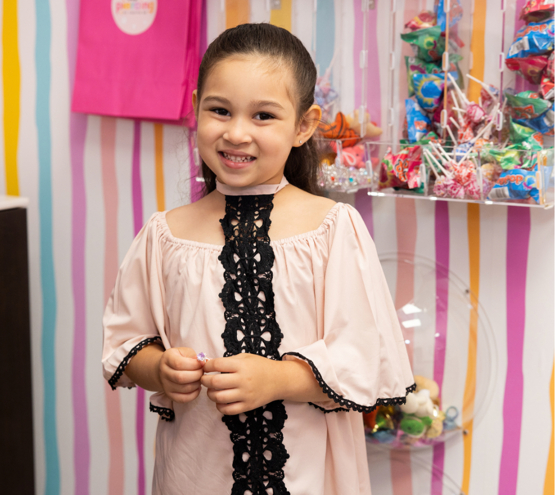 A young girl smiling at an ear piercing studio, holding a small prize.