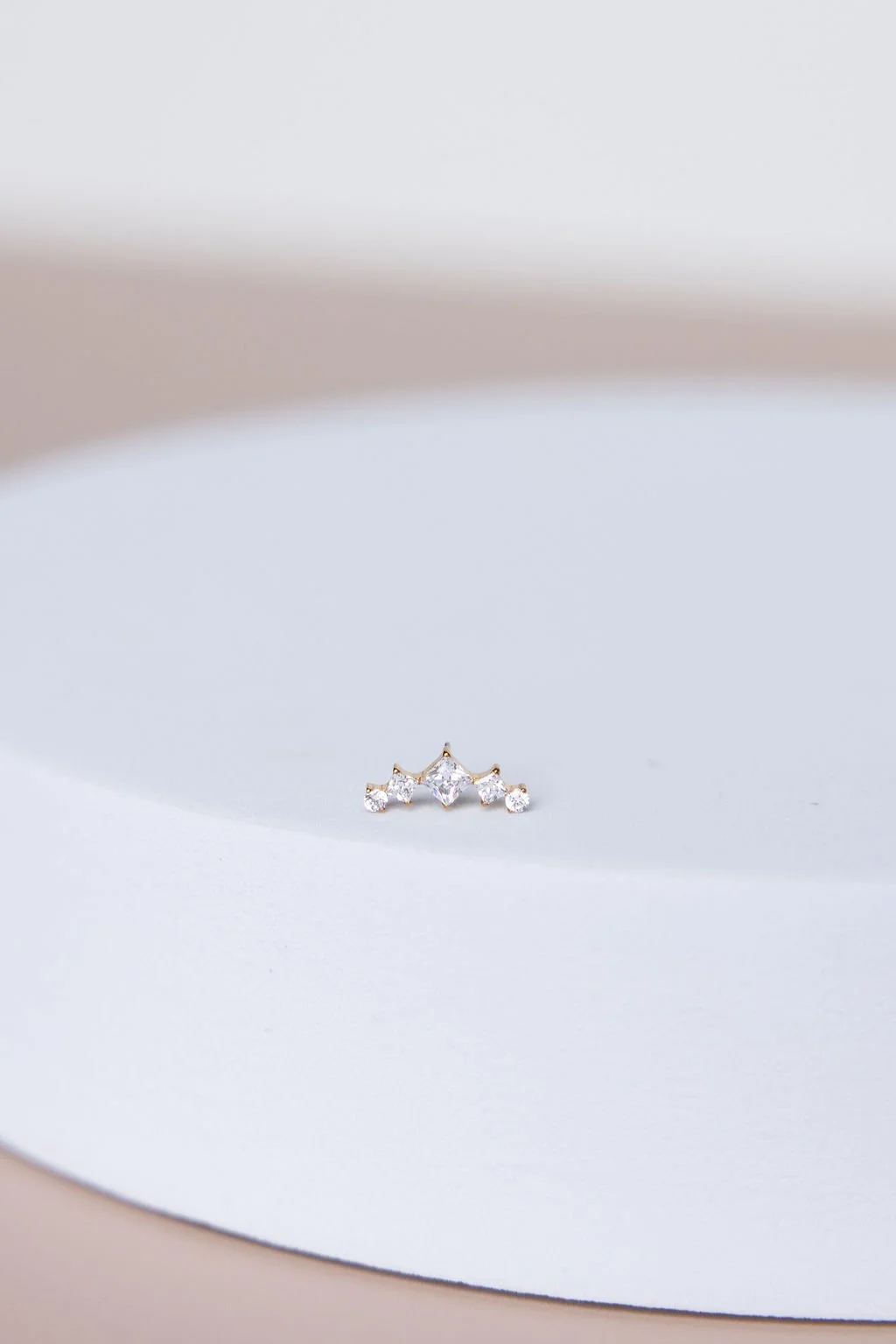 A small tiara-shaped jewelry piece with multiple clear gemstones on a white surface.