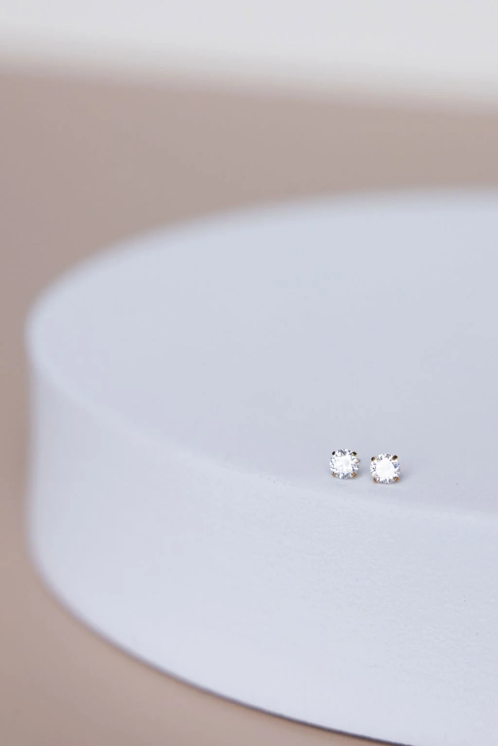 Pair of small diamond stud earrings on a white and beige curved surface.