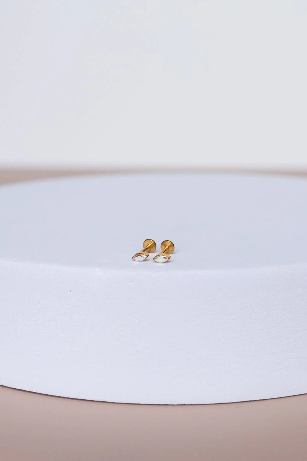 Pair of gold earrings with iridescent stones placed on white background.