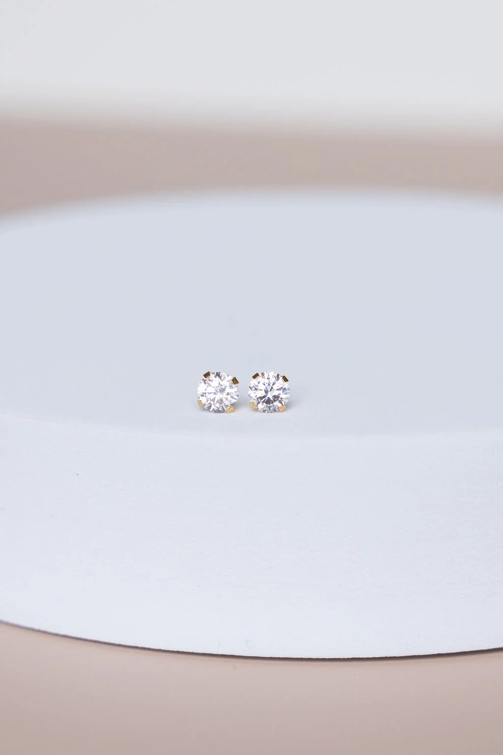 Pair of round diamond stud earrings on a white display surface.