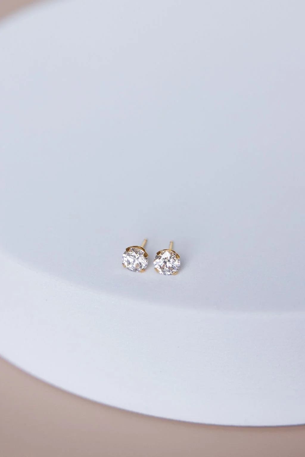 Pair of gold stud earrings with large clear gemstones on a white and pink background.
