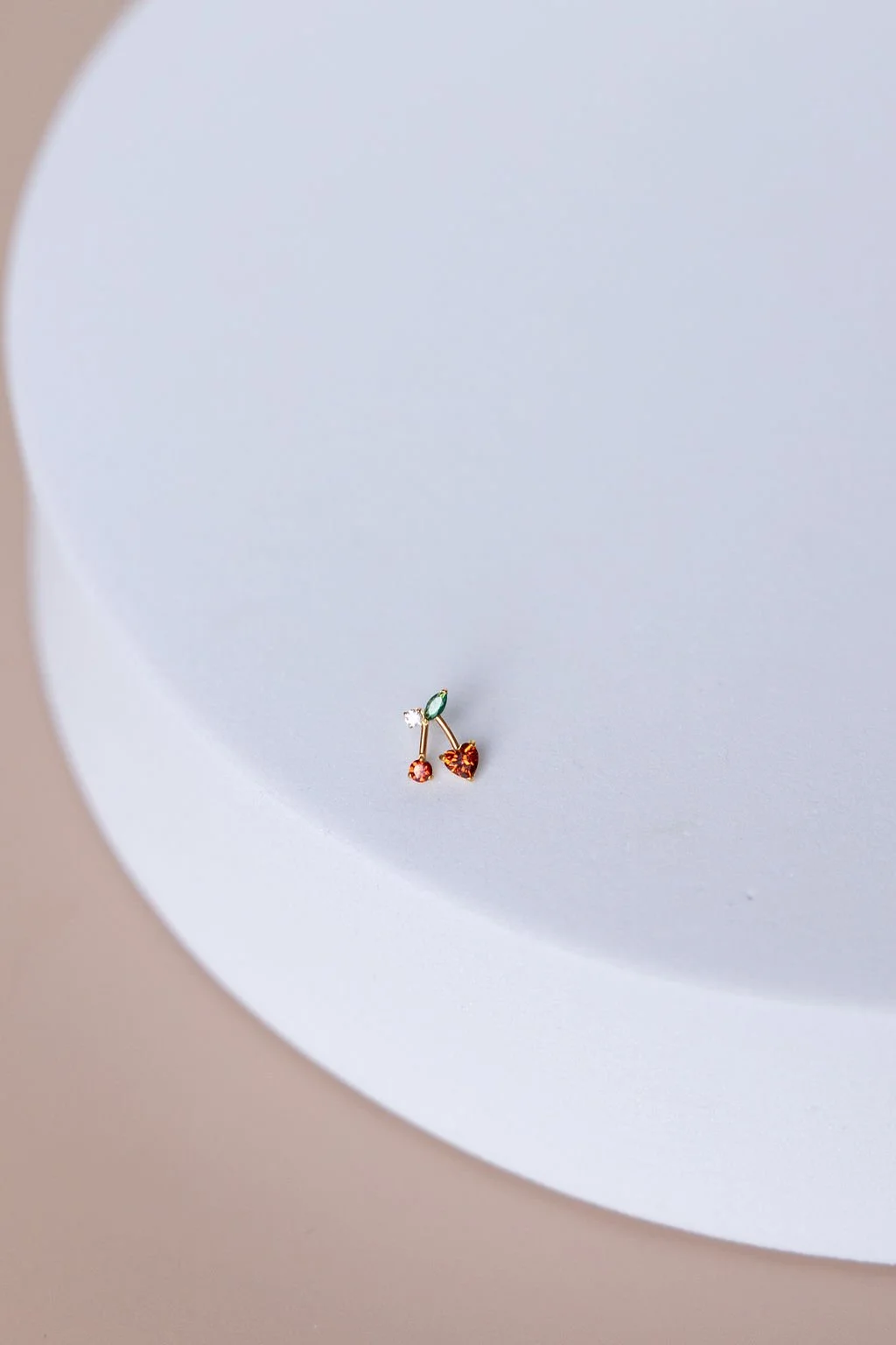 A close-up of a small, colorful, heart-shaped and round earrings on a white circular surface.