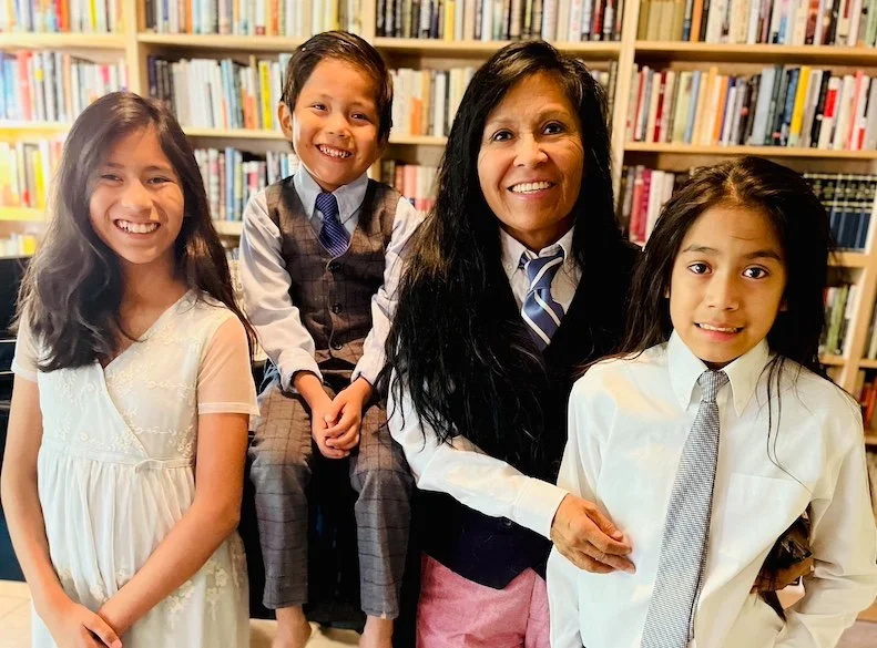 A woman surrounded by three young girls in a library with shelves of books in the background.