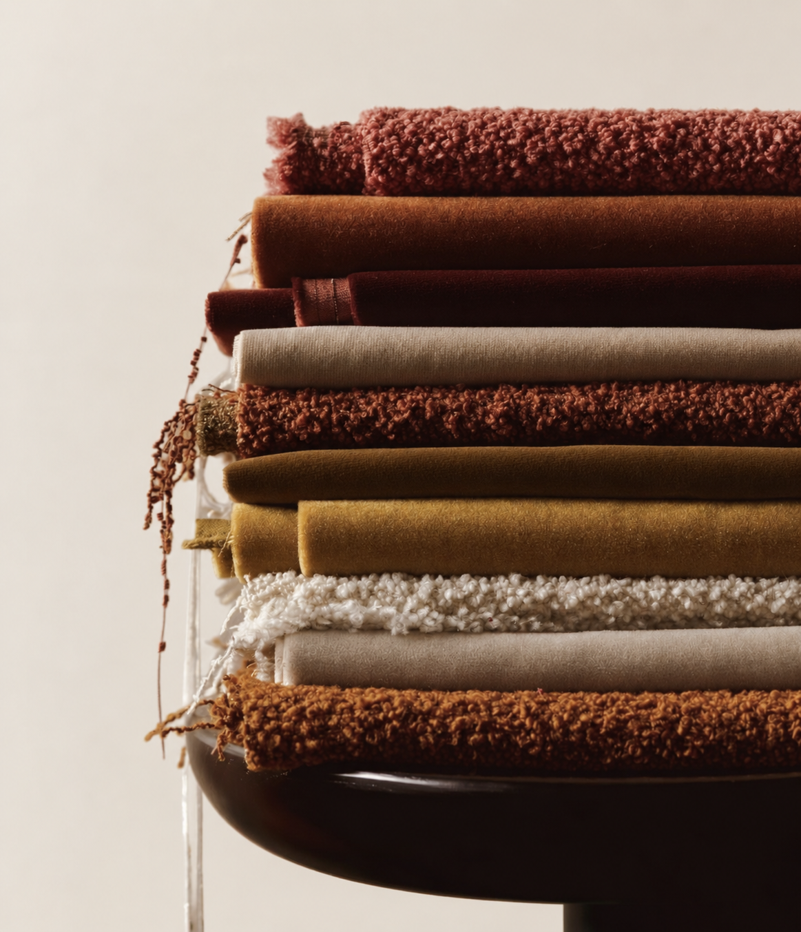 Stack of folded towels and fabrics in various warm earth tones on a side table.