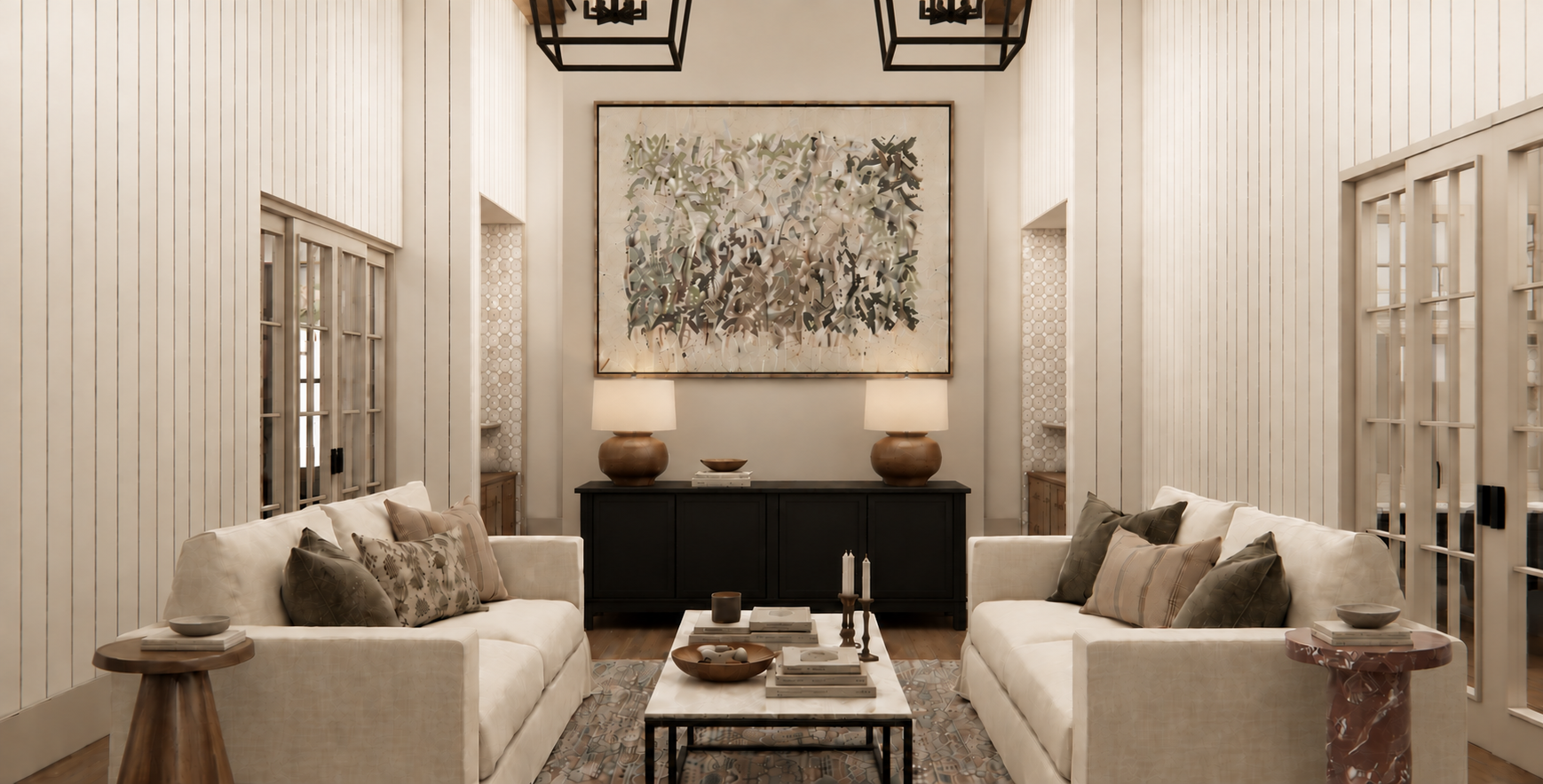 A cozy living room with white furniture, framed contemporary art, two table lamps, and a coffee table with books and decorative items.