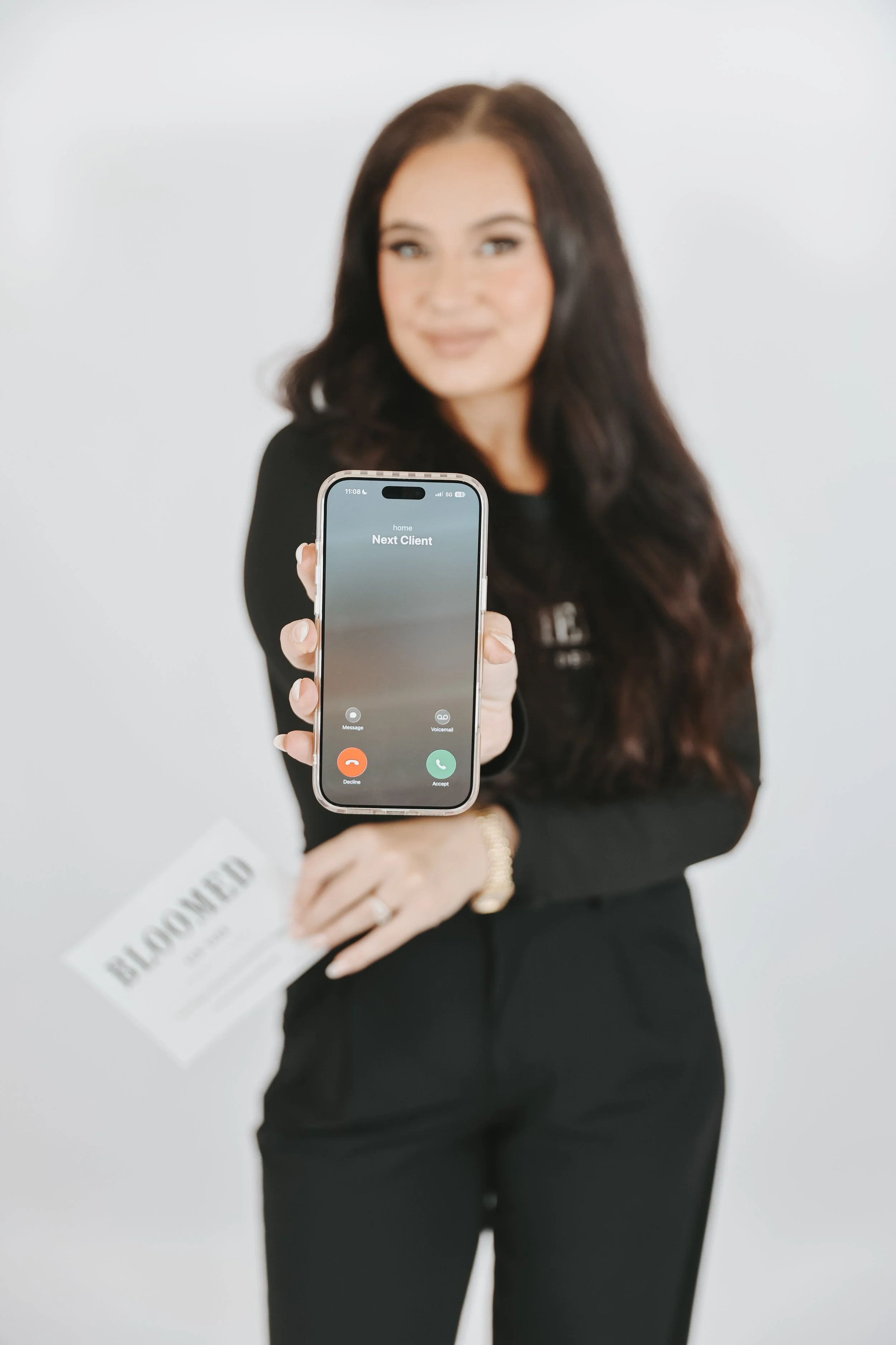 Woman in black outfit holding a smartphone with an incoming call display that says 'Next Client'.