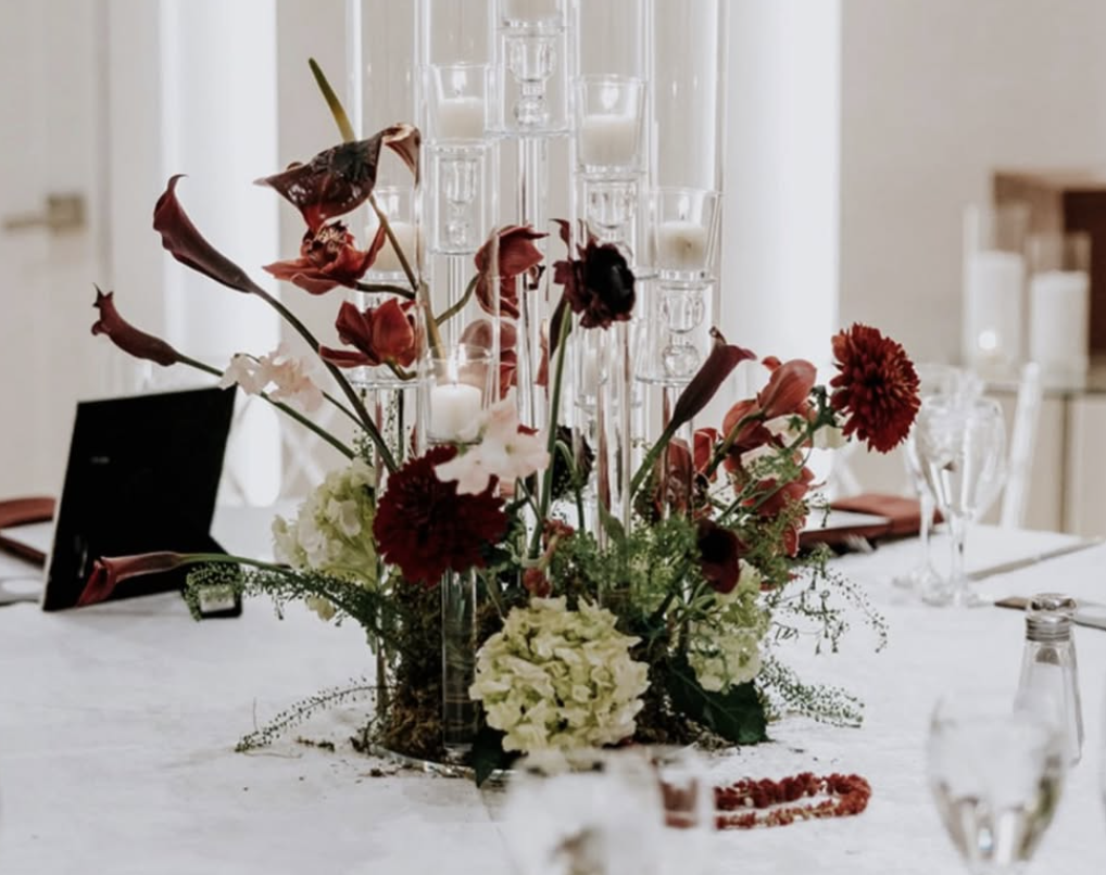 Elegant table centerpiece with red and white flowers, tall glass candle holders, and a white tablecloth at a formal event.