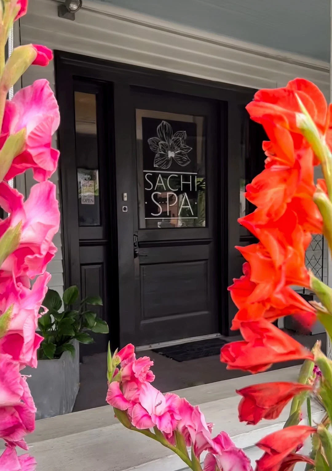 Entrance of Sachi Spa framed by pink and orange flowers.