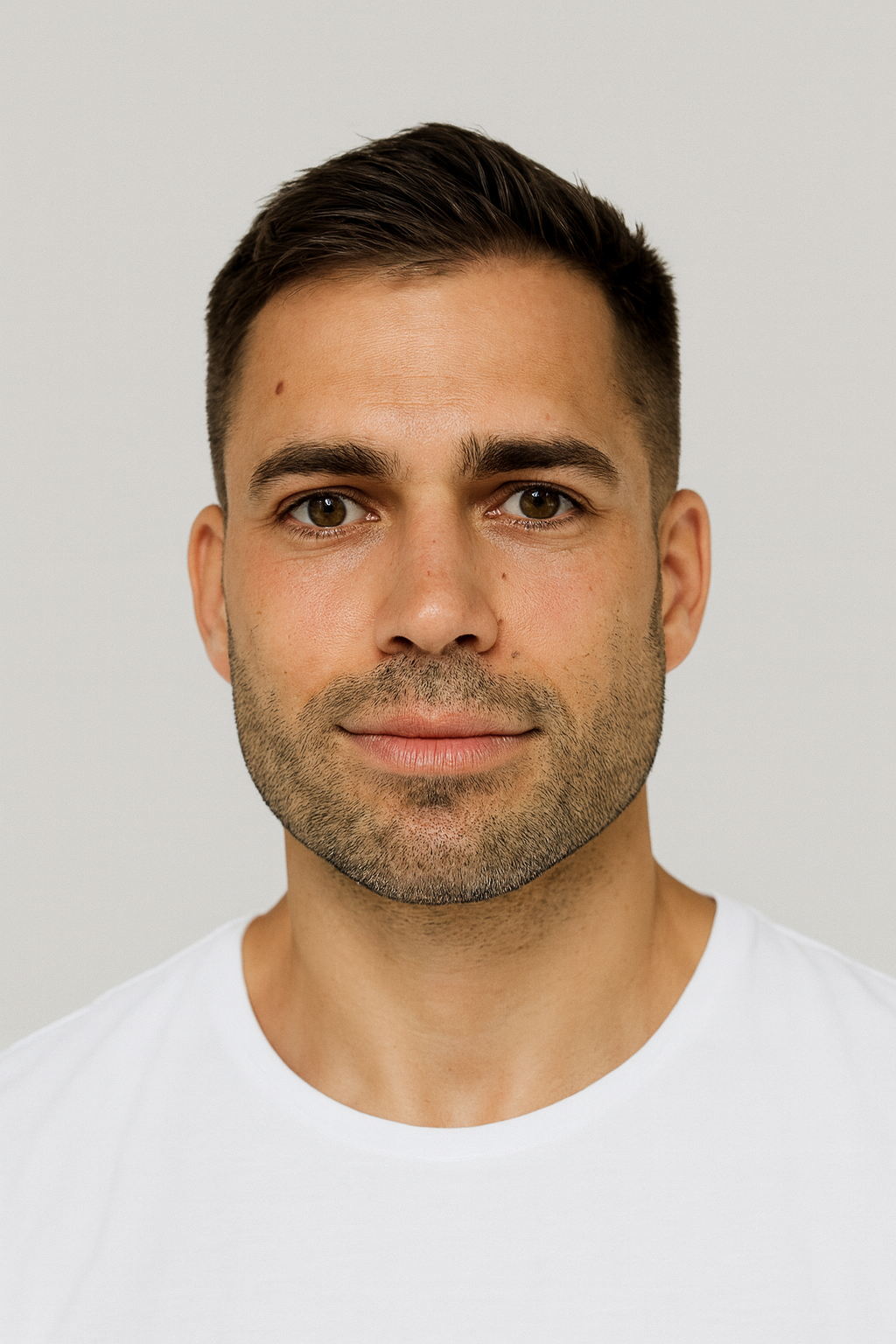 Close-up of a man with short dark hair and light skin, smiling slightly, wearing a white shirt.