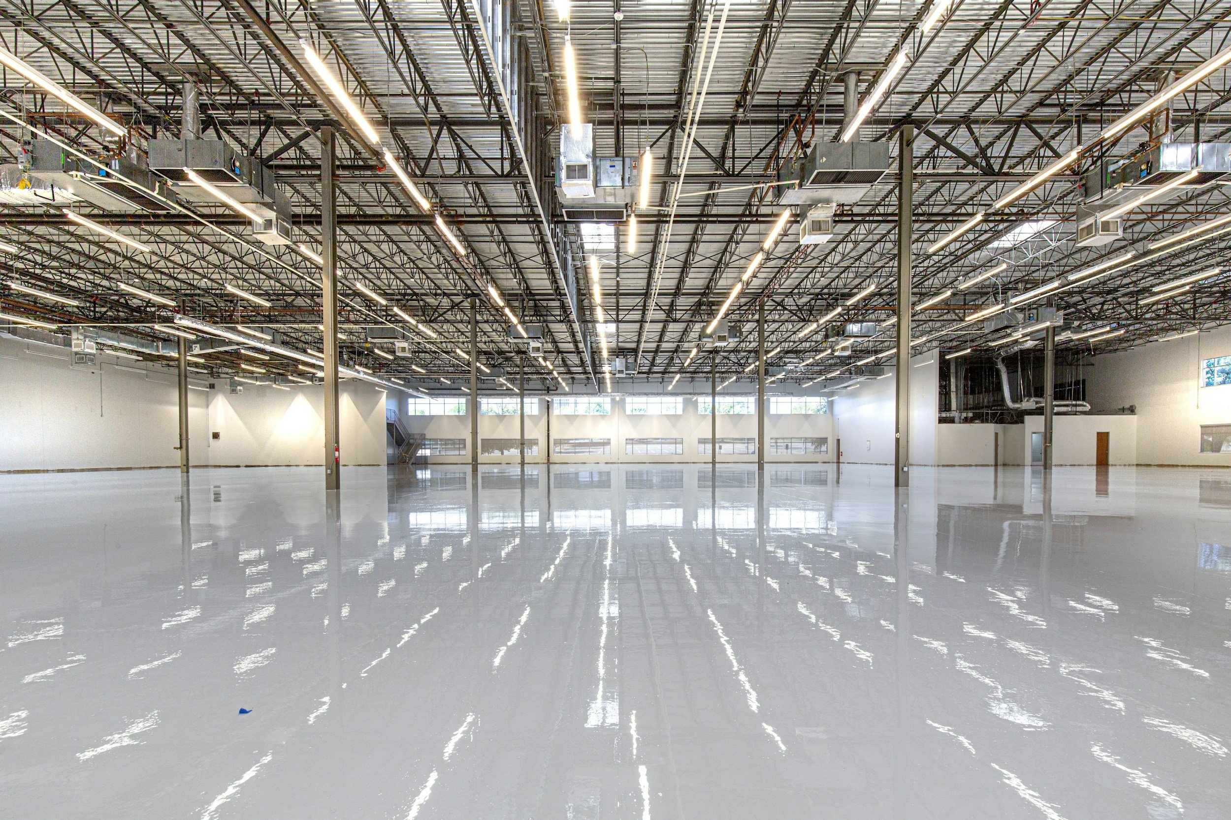 Empty industrial warehouse with bright overhead lighting and reflective polished floor.