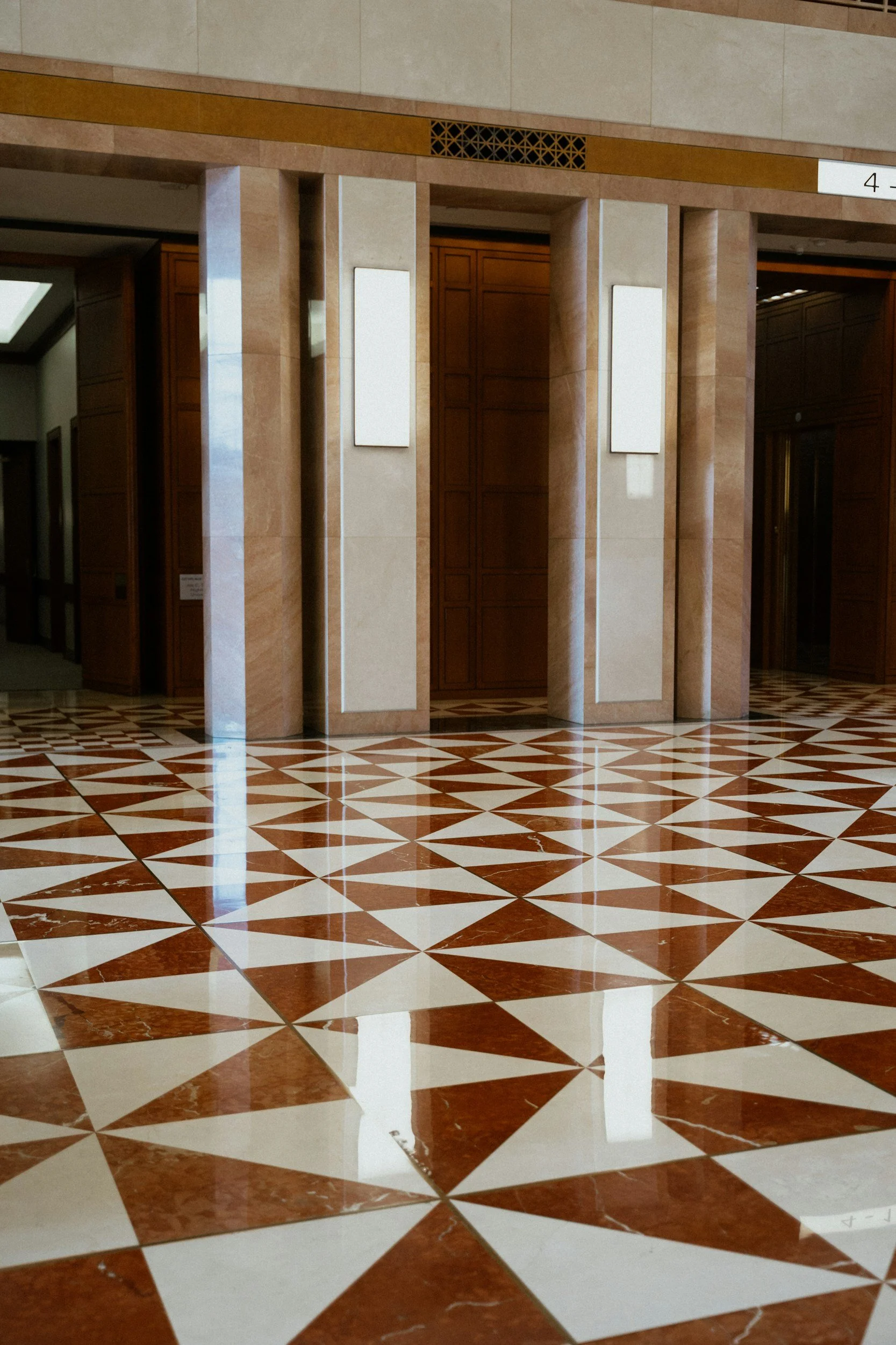 Interior view of a building with marble columns and a decorative tiled floor in geometric pattern, possibly part of an office or institutional lobby.