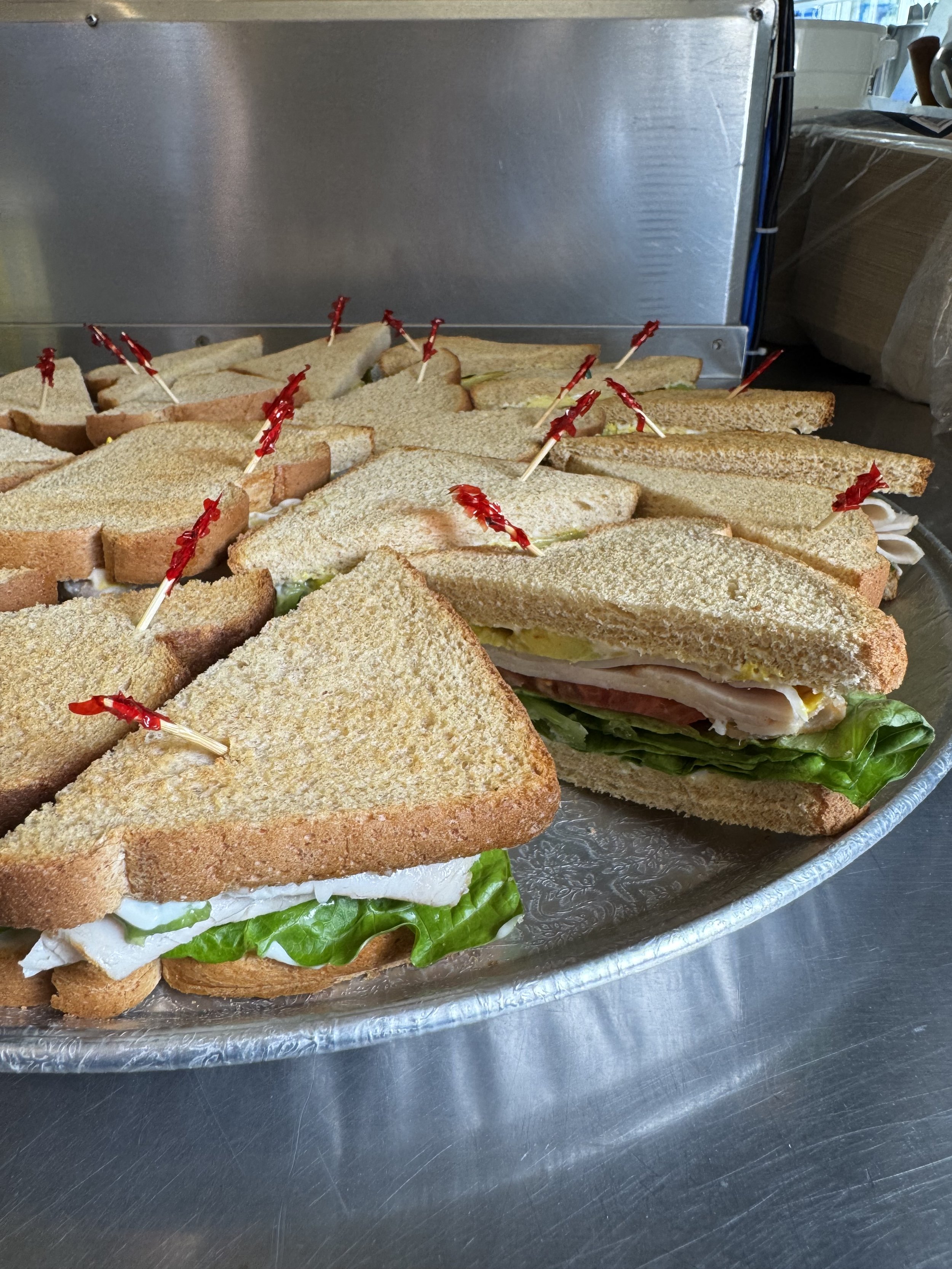 Assorted sandwiches on a tray, featuring various fillings such as lettuce, turkey, cheese, and possibly egg, with toothpicks for serving.