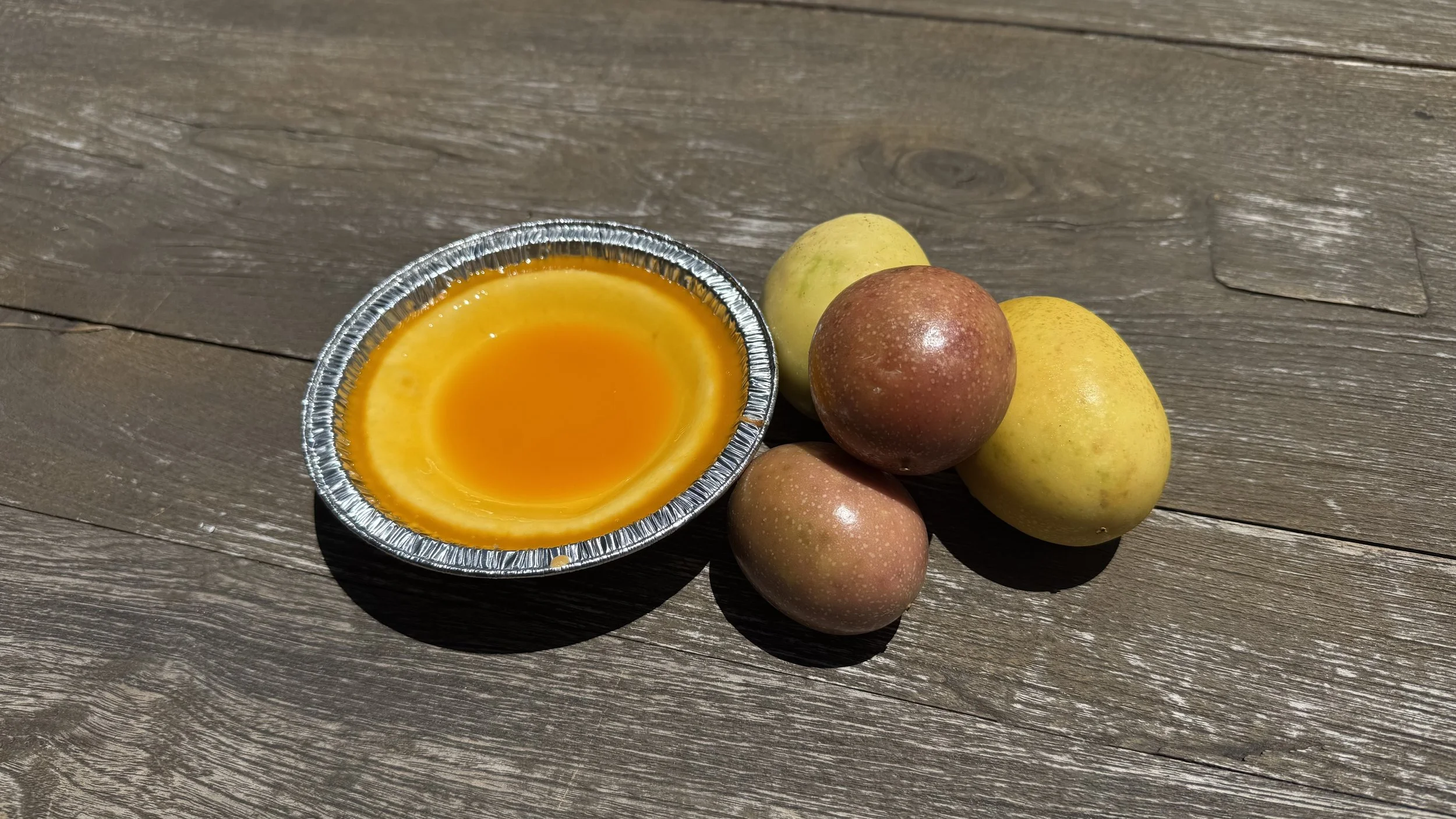 A small aluminum tray with a yellow-orange substance next to five peaches on a wooden surface.