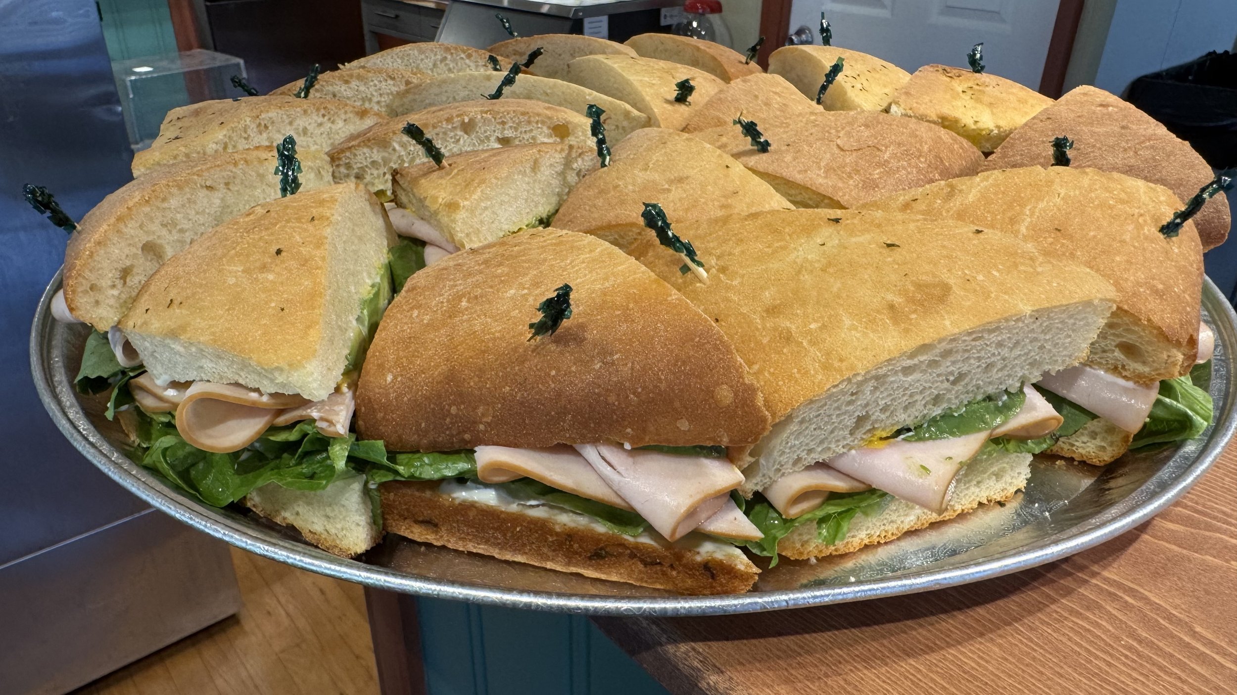 Large tray of sandwich bread stuffed with turkey, lettuce, and other ingredients, held together with black toothpicks.