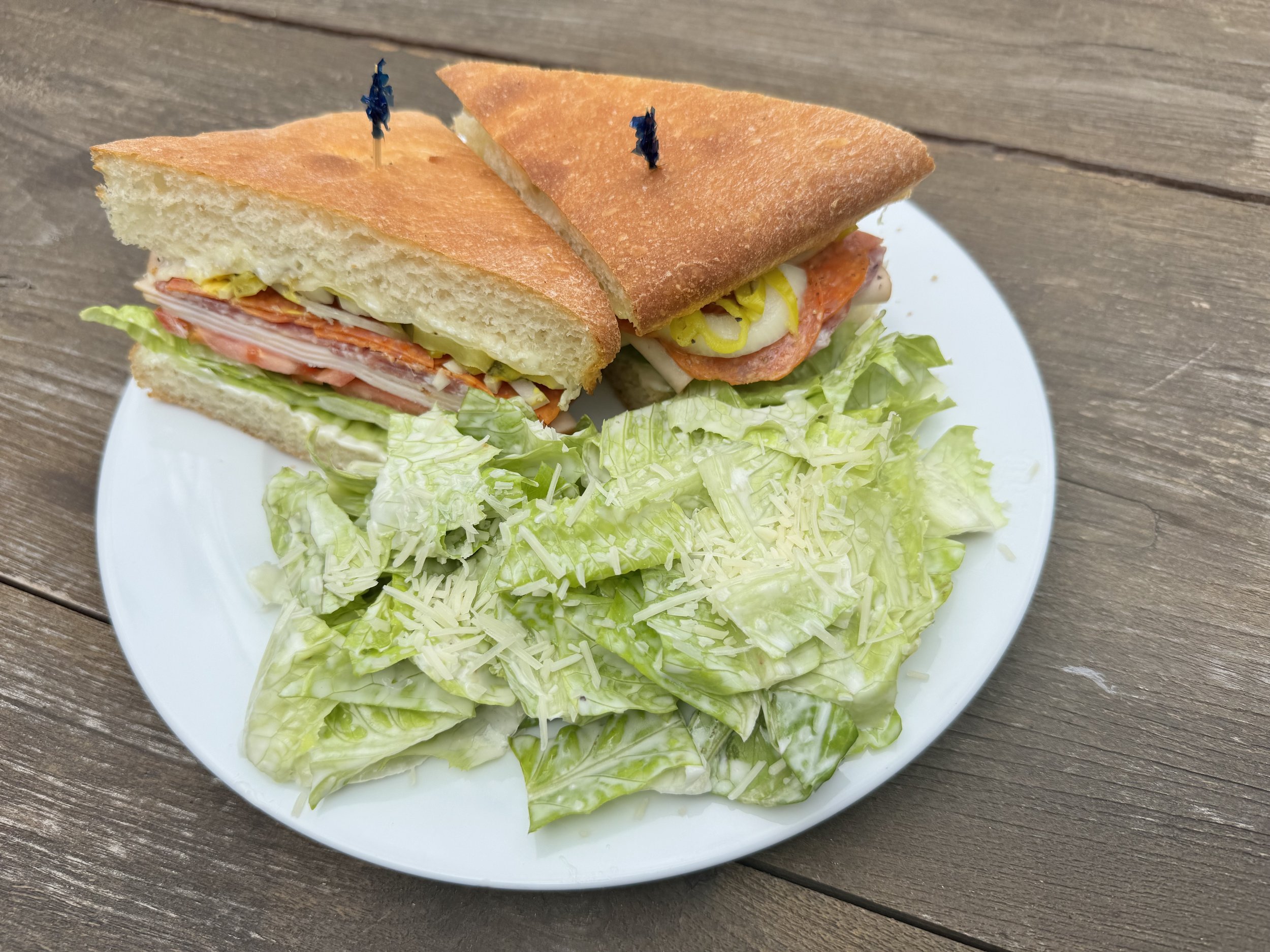Close-up of a sandwich on a white plate with shredded cheese and lettuce, placed on a wooden surface.