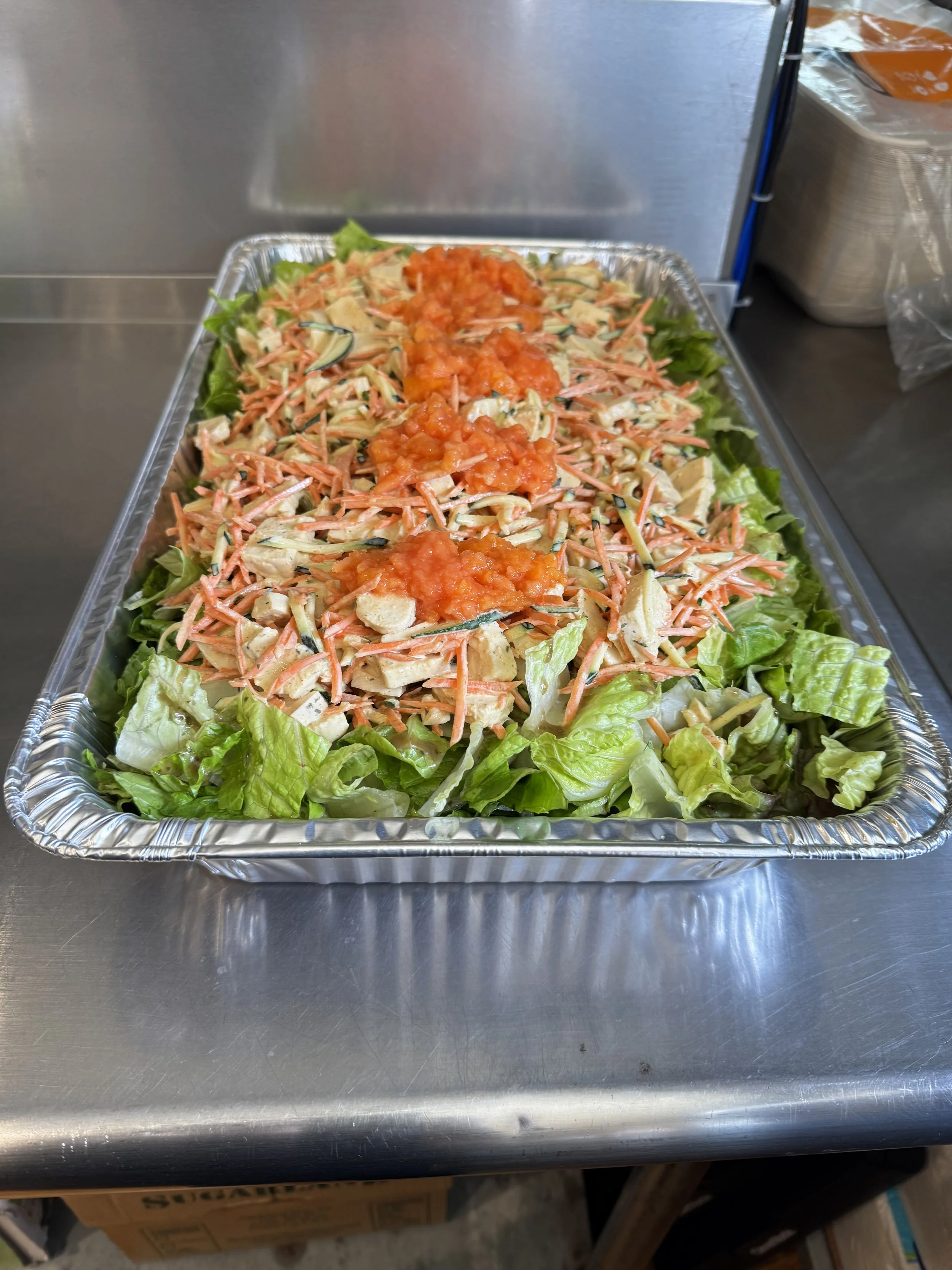 A tray of salad with lettuce, shredded carrots, sliced cucumbers, chopped chicken, and tomato sauce dolloped on top.