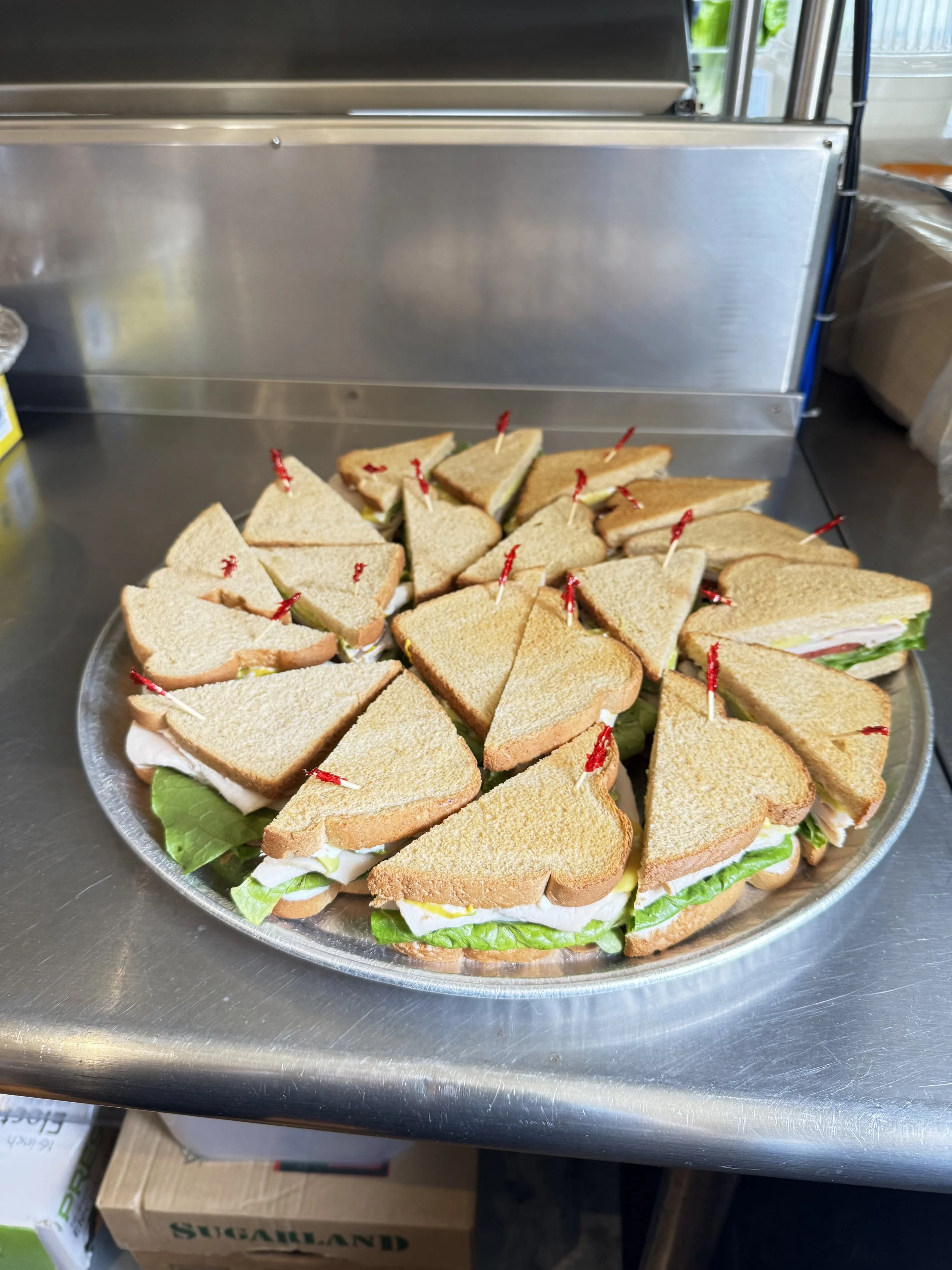 A large round tray of triangular sandwich snacks with lettuce visible, secured with red toothpicks, placed on a metal surface.